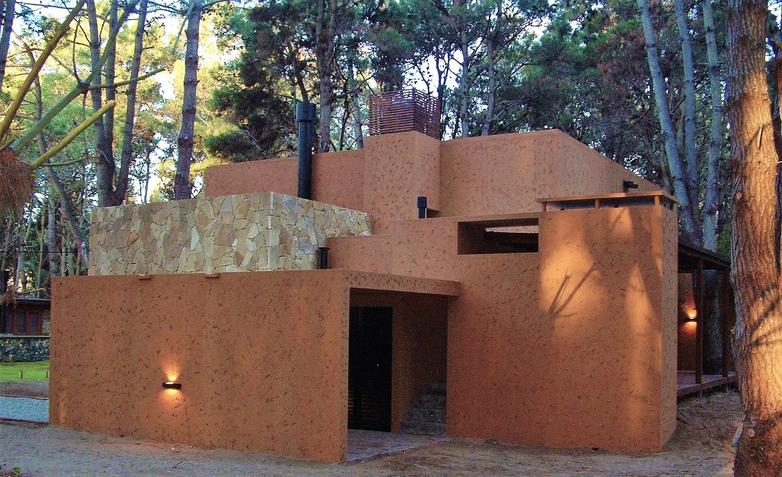 Fachada rústica moderna con detalles en piedra, rodeada de bosque — proyecto LA  ALHAMBRA, por GJF estudio, en Costa del Este