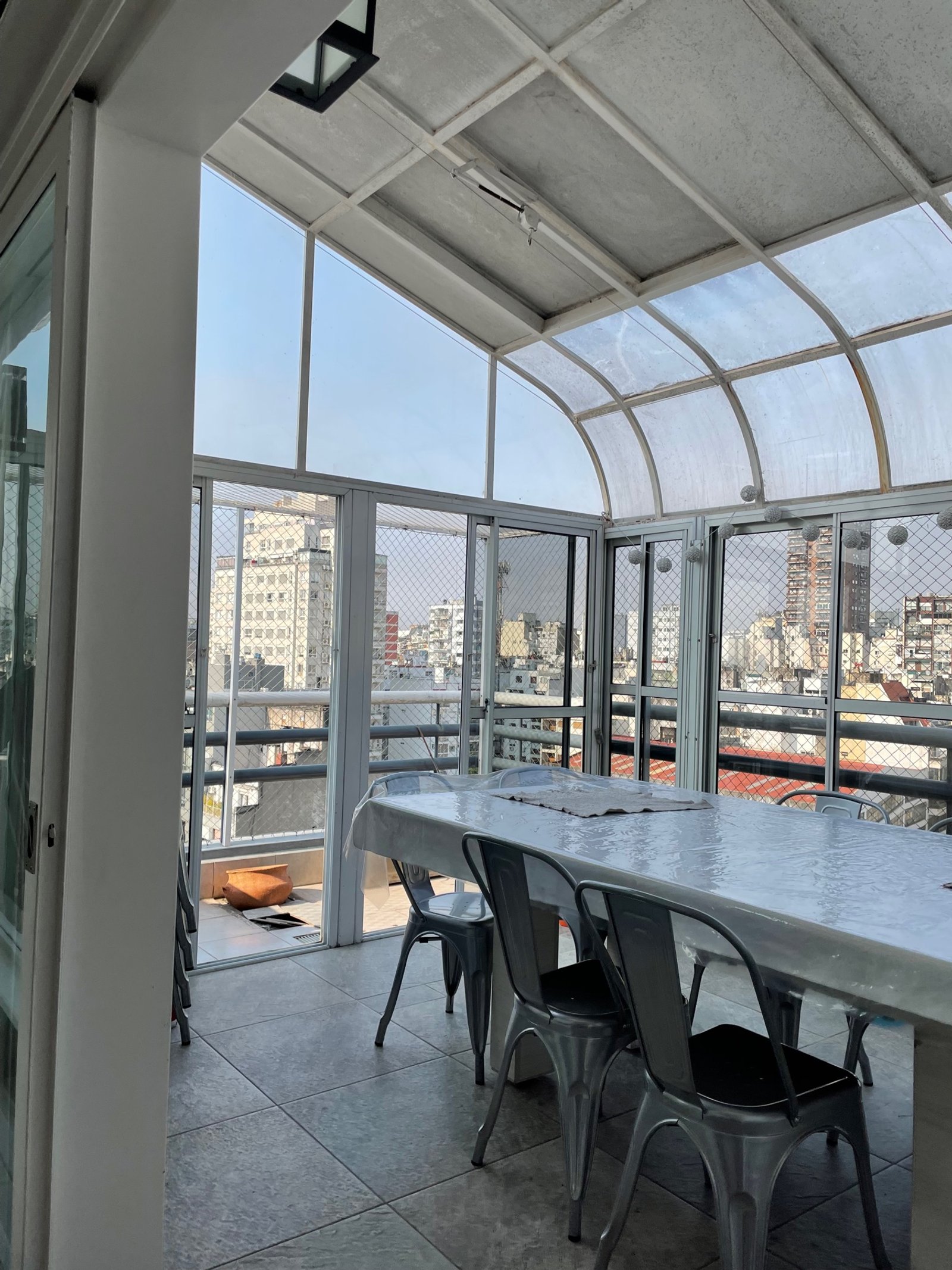 Comedor semi-exterior con techo transparente y vista urbana — proyecto Peña, por Estudio NET Arquitectura , en Peña 2726