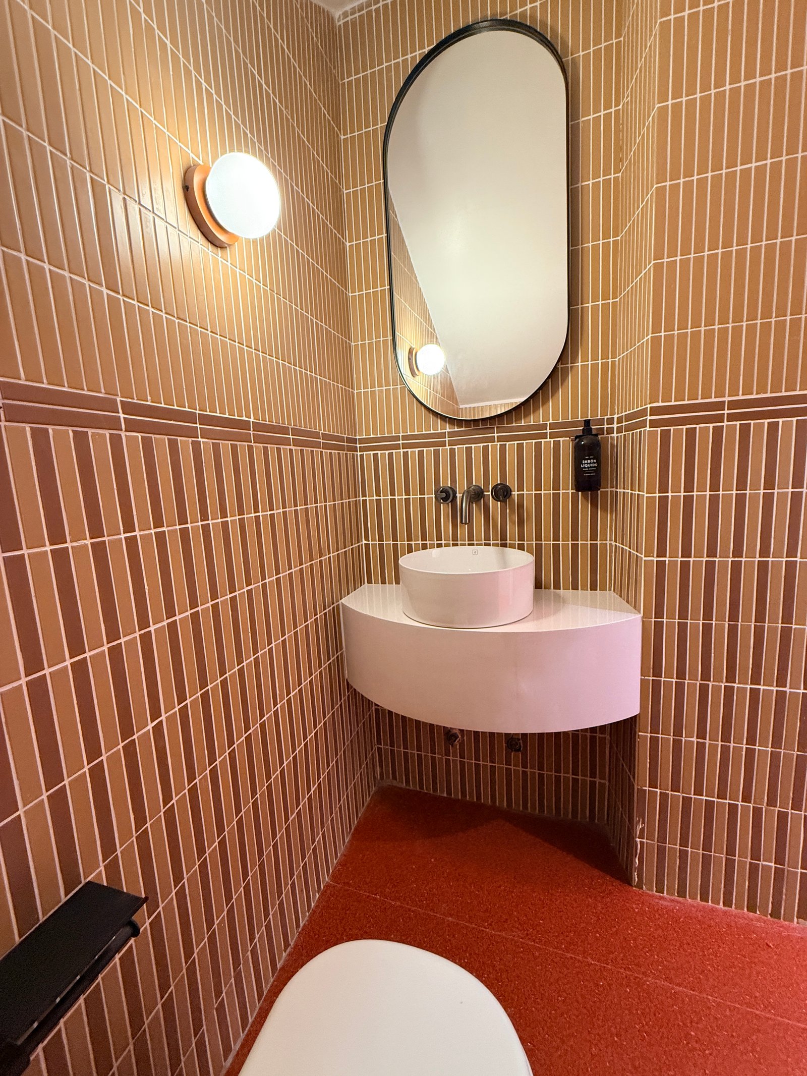 Baño moderno con azulejos verticales terracota y lavabo curvo — proyecto Lunático, por Estudio Losa, en Av. Corrientes 1659