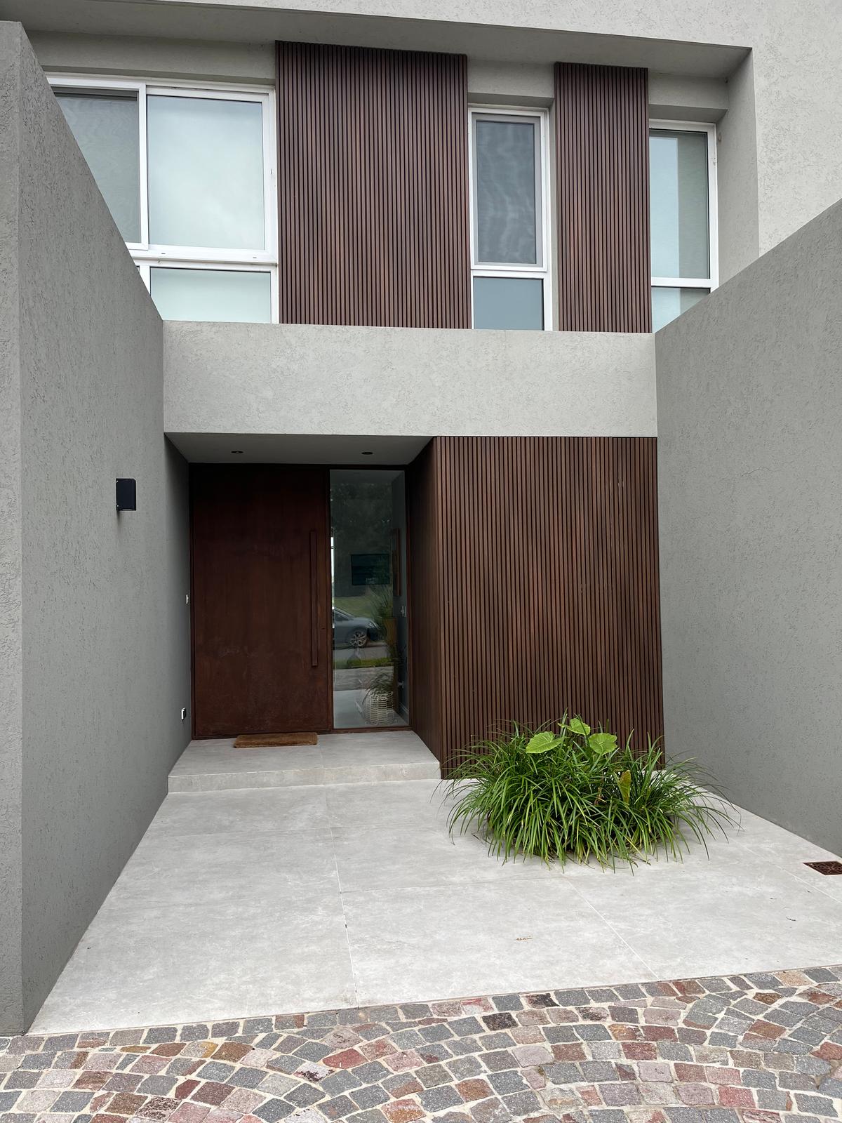 Fachada moderna com porta pivotante de madeira escura e detalhes de ripas — projeto SAN MATIAS II, por Fb Arqs, em Belén de Escobar