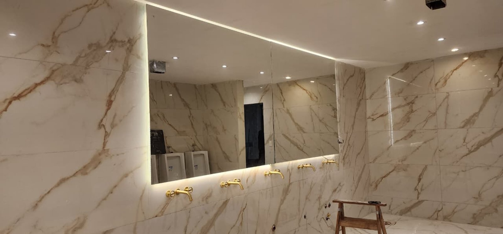 Baño comercial con paredes de mármol veteado, espejo grande y grifería dorada — proyecto BNA CENTRAL ESPEJOS LED, por Cristalcenter, en Centro