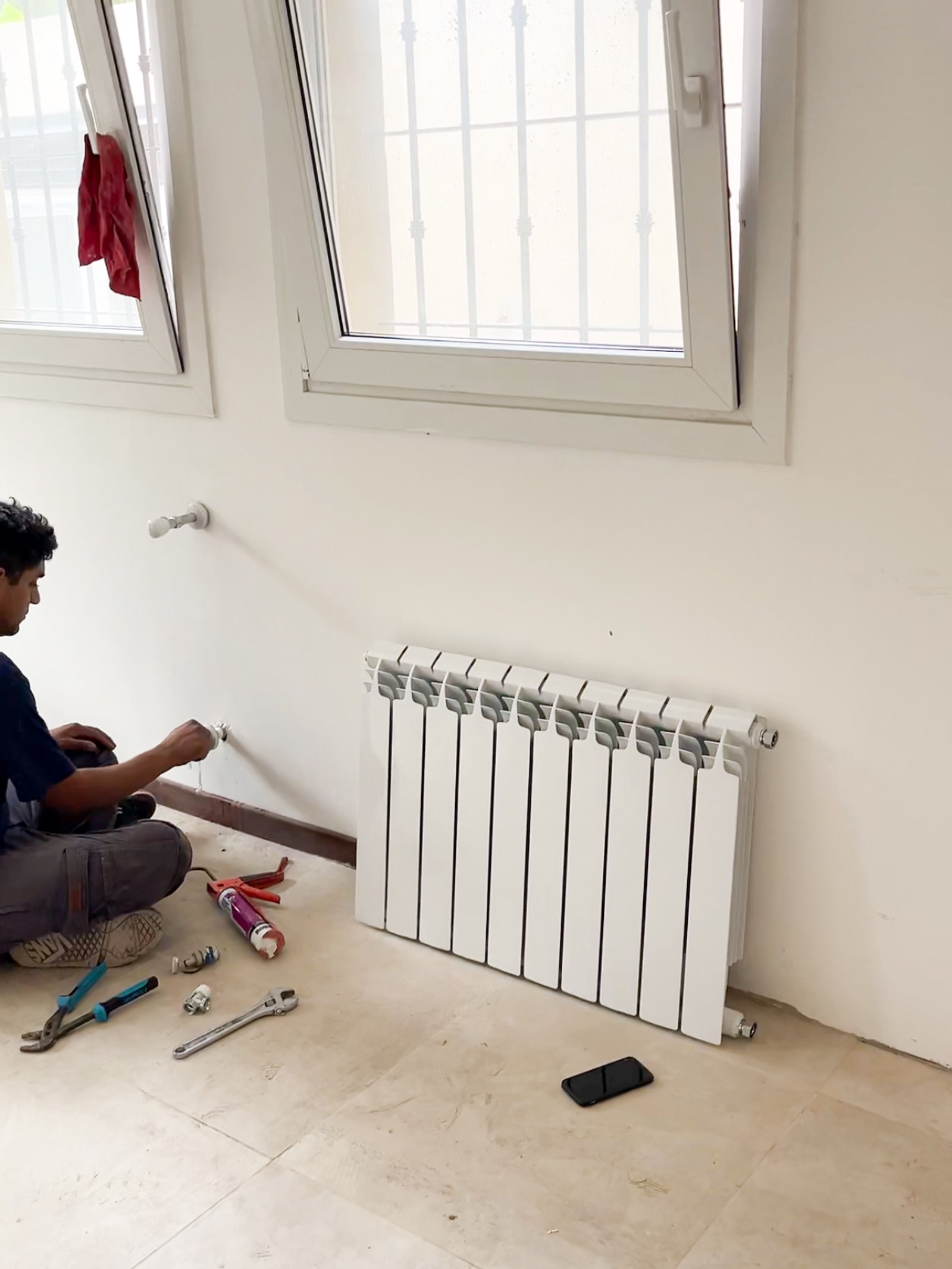 Instalación de radiador con herramientas y celular en piso — proyecto Instalación de Radiadores en Tigre, por Climatizacion HD, en B1648 Tigre