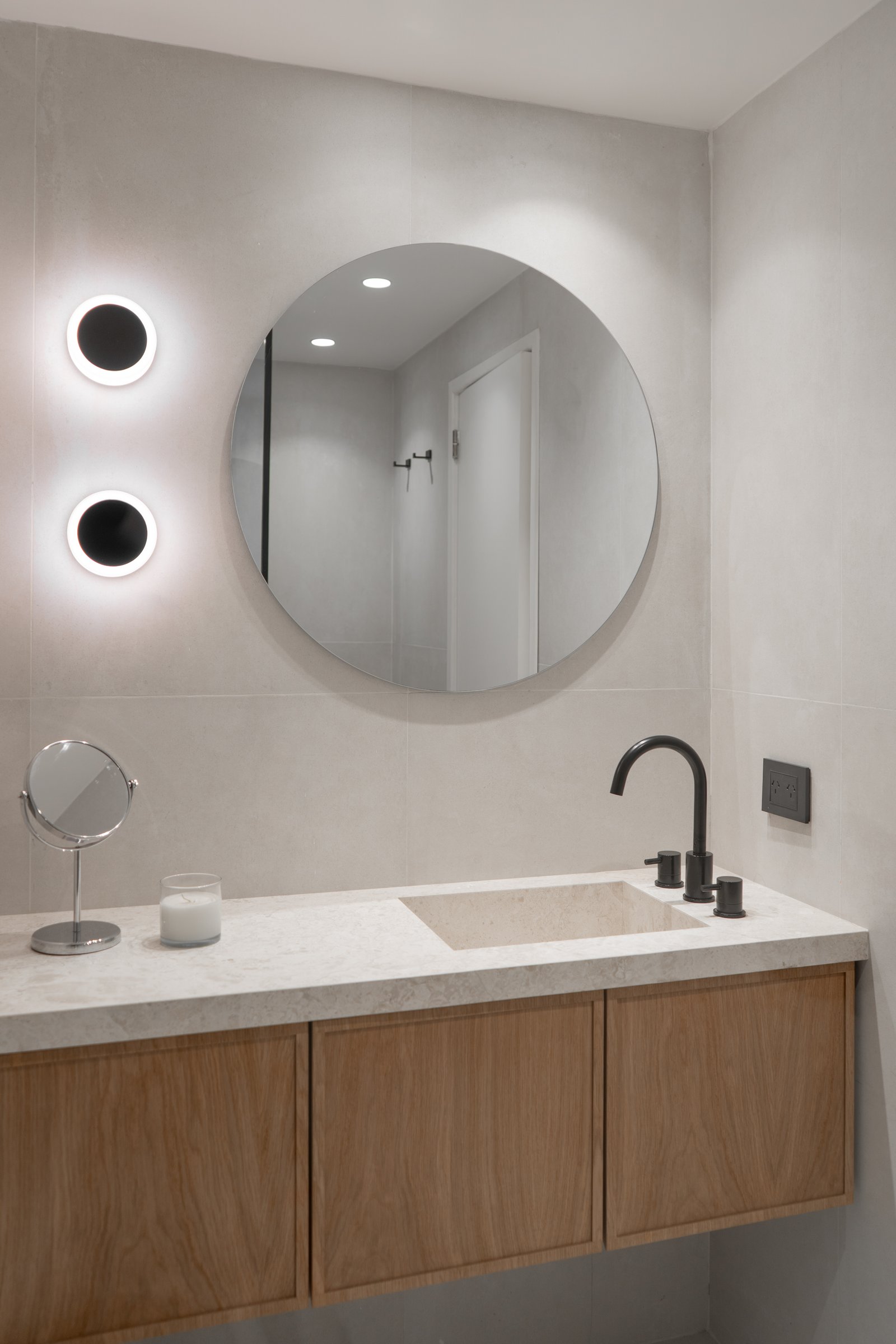Baño moderno minimalista con vanitory de madera flotante y espejo redondo — proyecto Juana manso , por KUPERDESIGN CONSTRUCCIONES SRL, en Juana Manso 740
