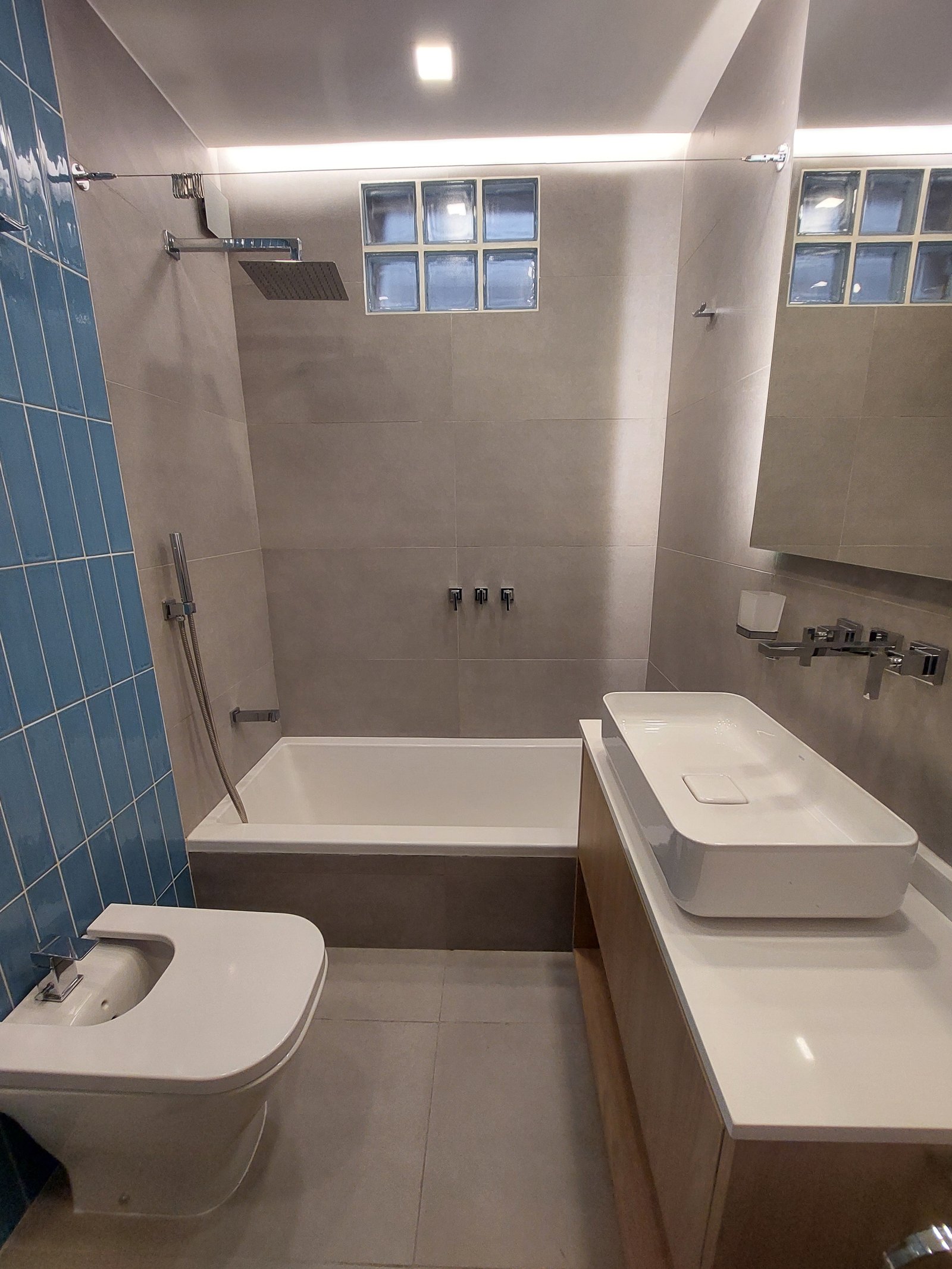 Baño moderno con bañera exenta, bacha lineal y revestimientos grises y madera — proyecto FLORES, por Arquitecta, en Flores
