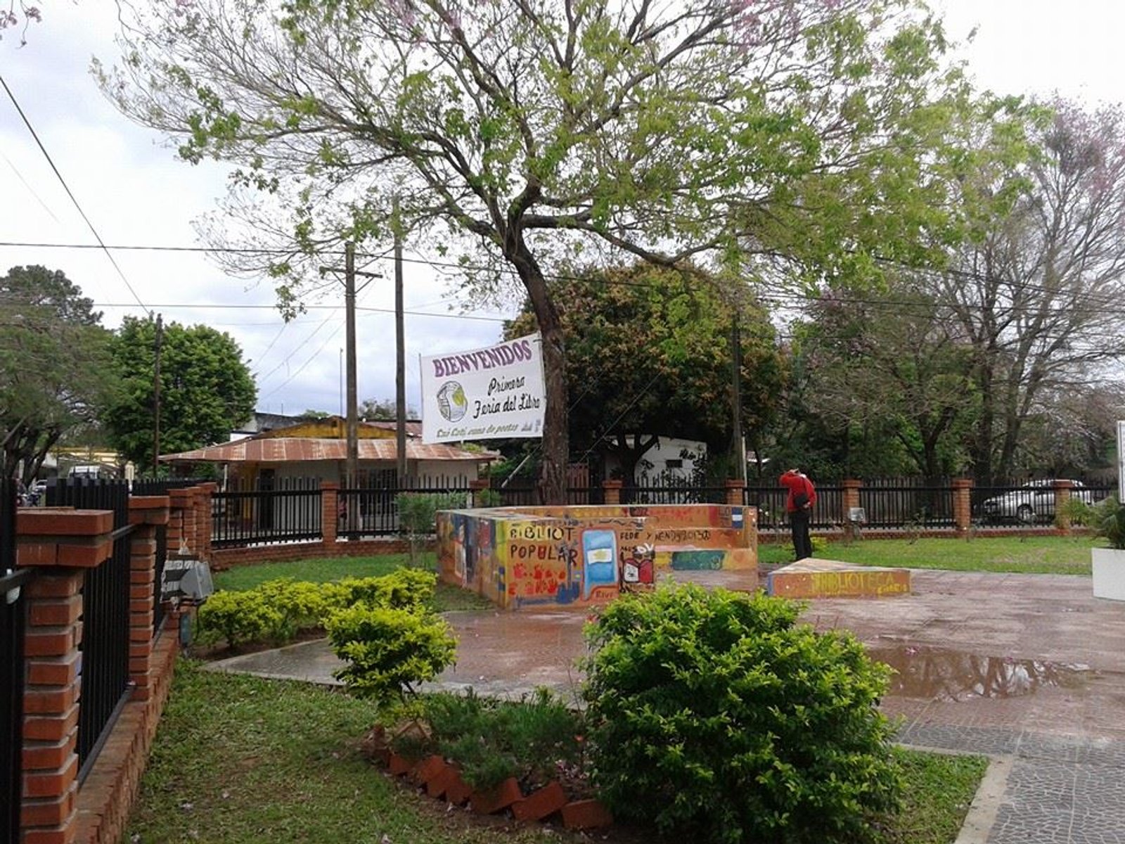 fachada comercial com banner grande e árvore — projeto Biblioteca Publica, Dr. Juan Manuel Rivera. Caa Cati, Corrientes., por Arquitecto Gustavo Maidana, em Caá Catí