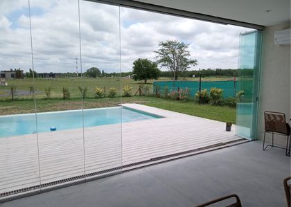 Pileta moderna con deck de madera y vista al campo abierto — proyecto LAS PRADERAS DE LUJAN, por CERRAMIENTOS PANORAMICOS, en Luján