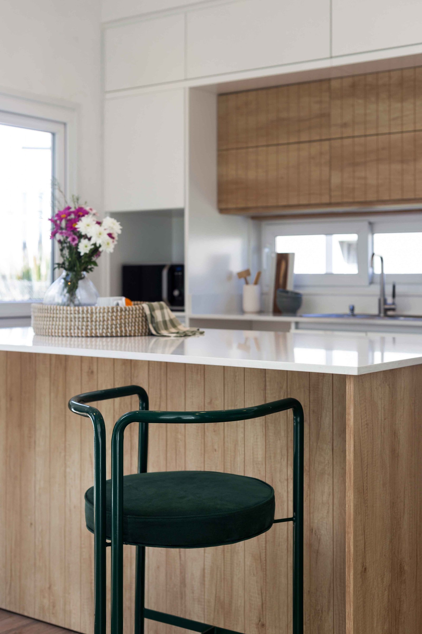 Cozinha moderna com ilha, banco de bar verde e detalhes em madeira — projeto SANTA INÉS I, por Estudio Stepa, em Canning