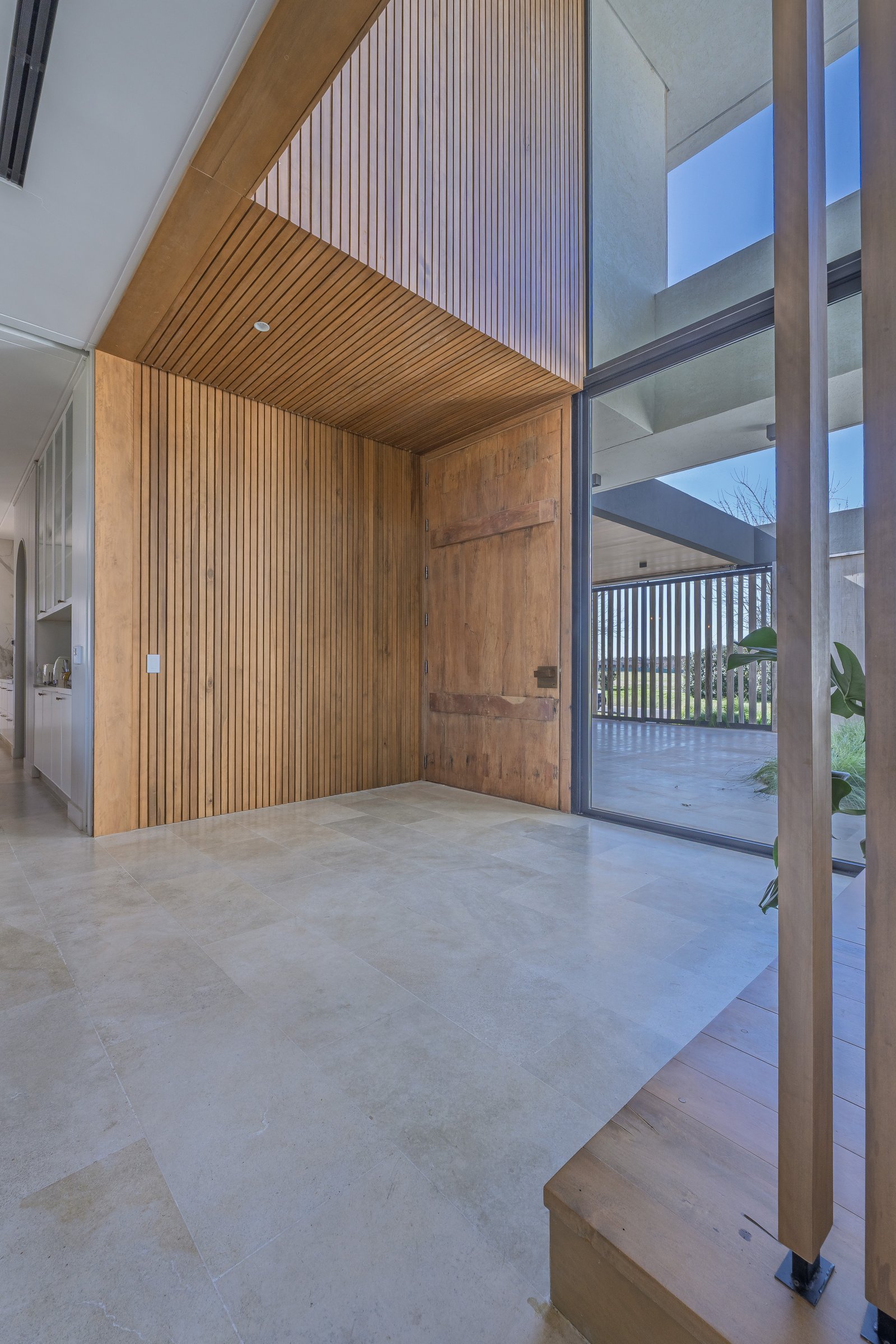 Entrada moderna con puerta pivotante de madera y pared de listones — proyecto Pilar A, por Josefina Bertora, en Los Cipreses 2