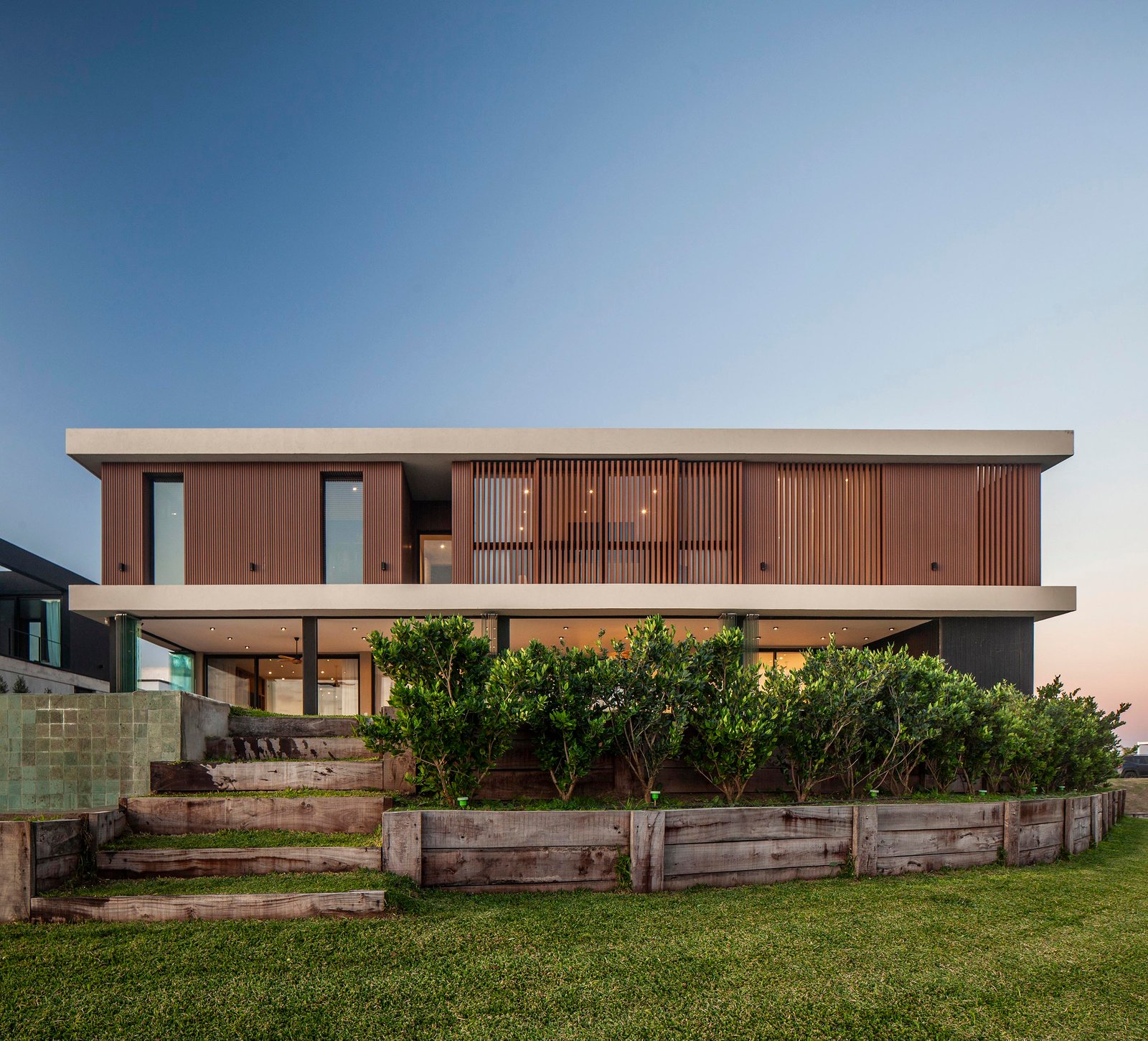 Fachada moderna de casa con revestimiento de madera y amplios ventanales frente al mar — proyecto CASA C313, por A'PRIMA - Arquitectura Sustentable, en Provincia de Buenos Aires