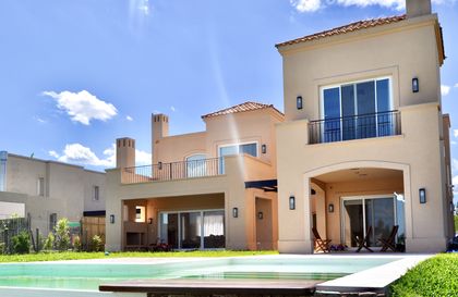 Casa moderna beige con pileta azul y grandes ventanales — proyecto Santa Catalina, Villanueva, por Marconi Silva Arquitectos, en Benavidez