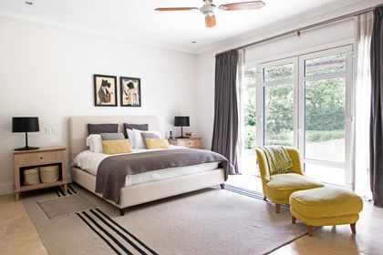 Dormitorio moderno con cama gris, sillón amarillo y ventanal luminoso — proyecto La Chacra , por Estudio Du 