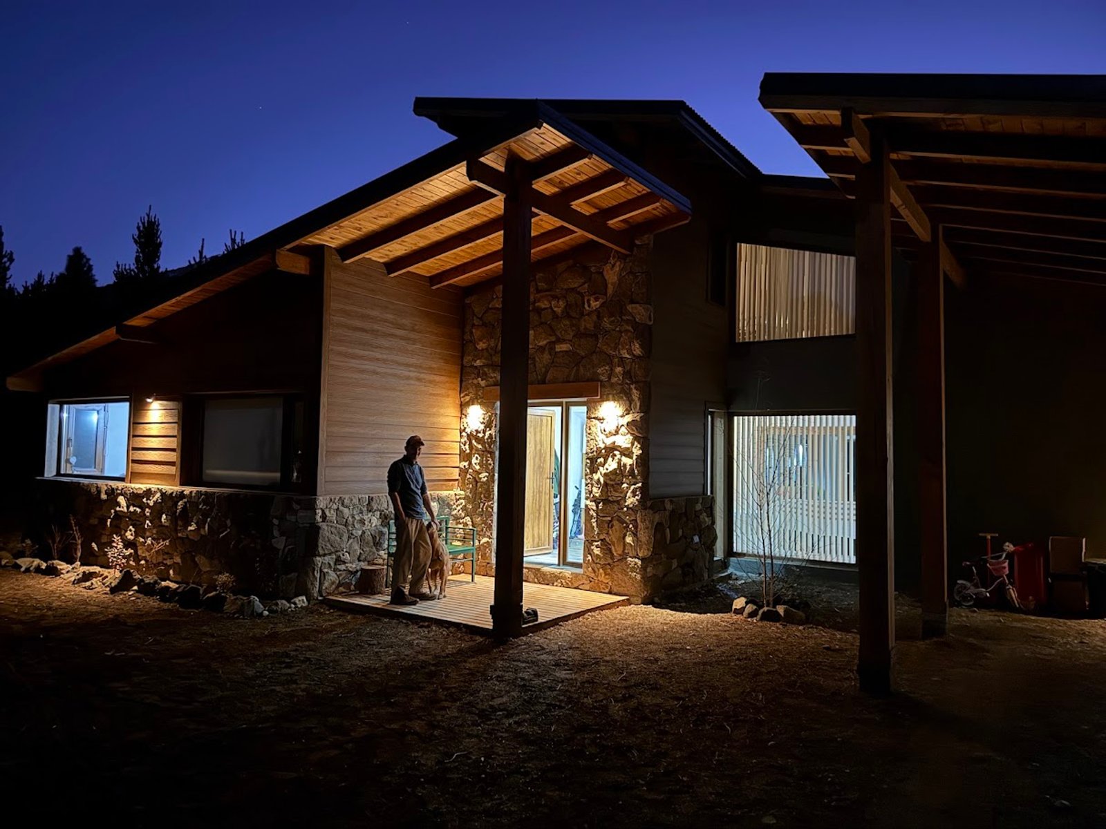 fachada de casa moderna rústica iluminada à noite — projeto Proyecto Casa SZ, por Arquitecta Grace Overgaard, em Acceso Al Challhuaco