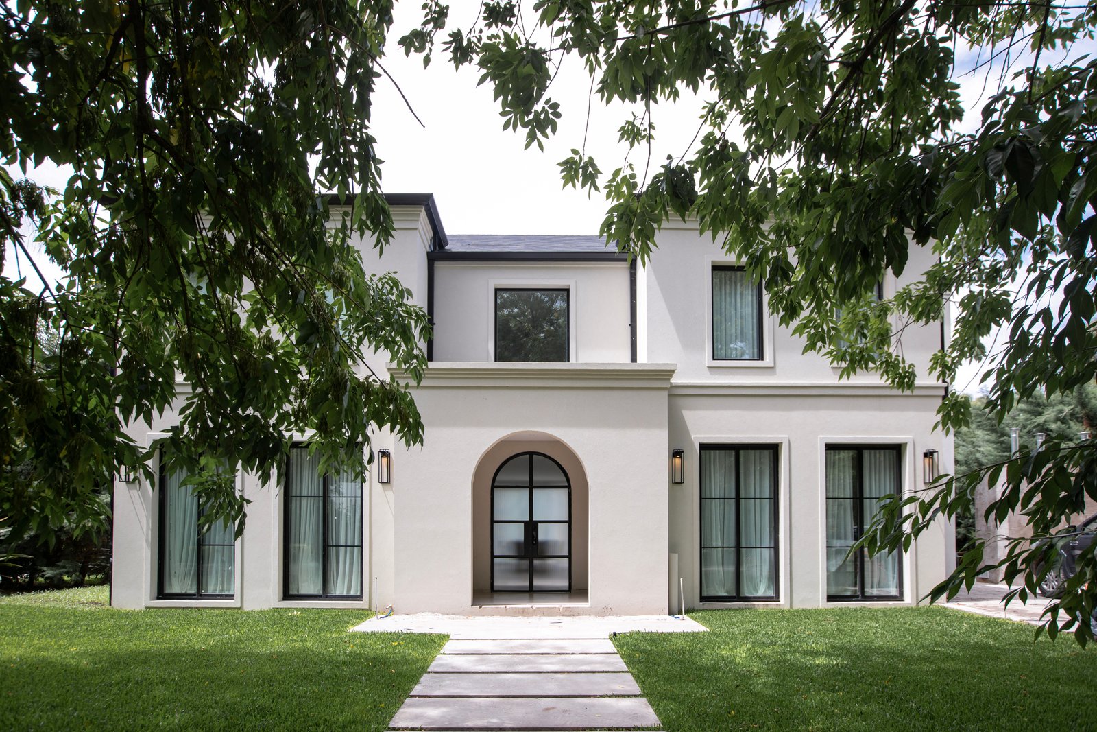 Fachada moderna blanca con arcos y vegetación exuberante — proyecto OBRA TRAVERTINO BEIGE, por ILVA, en Provincia de Buenos Aires