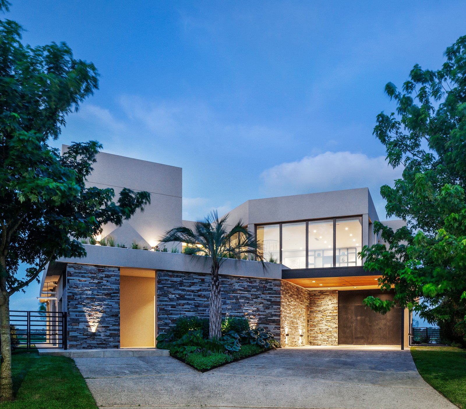 Fachada moderna de casa con piedra y vidrio al atardecer — proyecto CASA M40, por A'PRIMA - Arquitectura Sustentable, en Unnamed Road