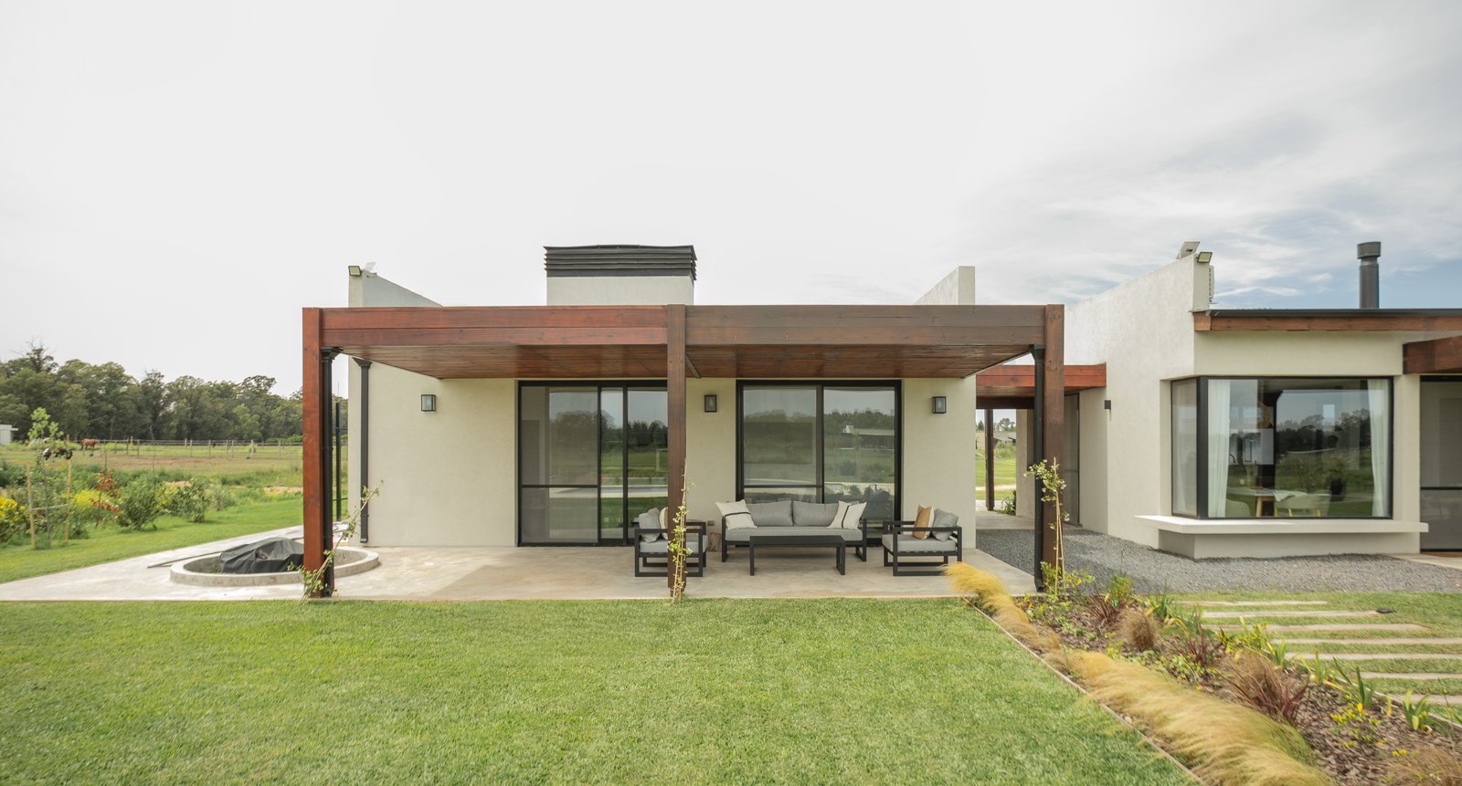 Fachada moderna de casa rural con pérgola y sala exterior — proyecto CASA AB, por SEDE Arq., en Av. Pereda S/N