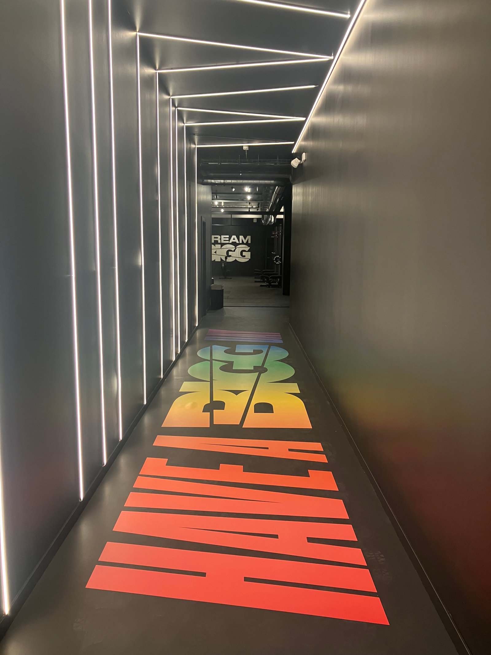 Pasillo moderno con luces indirectas y texto arcoíris en el suelo — proyecto BIGG EIXAMPLE, por GeN Arquitectura, en Carrer del Consell de Cent