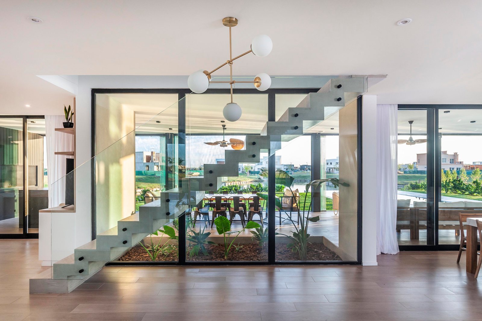 Escada flutuante moderna com janelas altas e luminárias pendentes — projeto CASA C313, por A'PRIMA - Arquitectura Sustentable, em Provincia de Buenos Aires