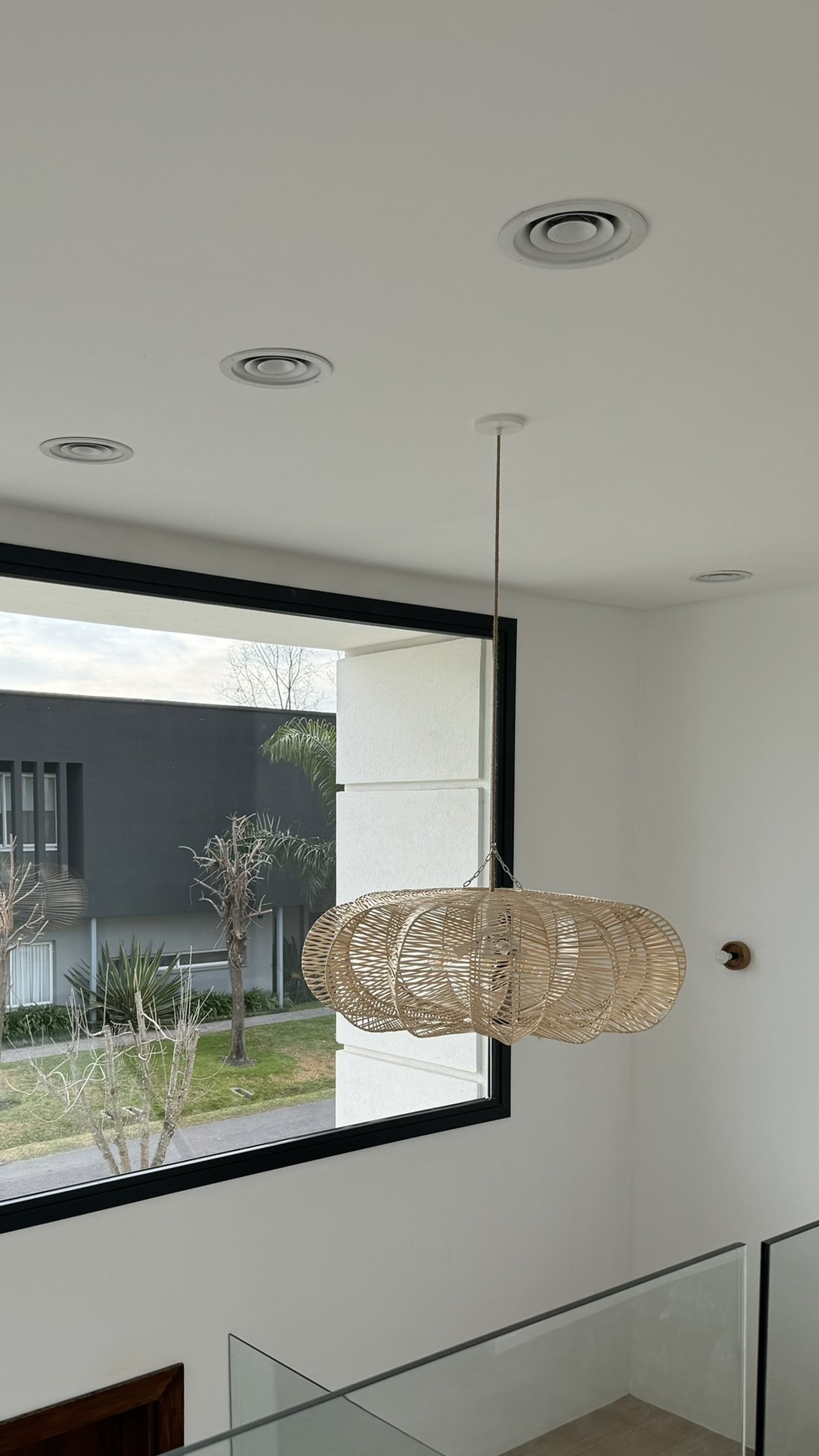 Interior de escada moderna com lustre de vime e janela grande — projeto Casa MC, por Hermann Arquitectos, em Bv. Central