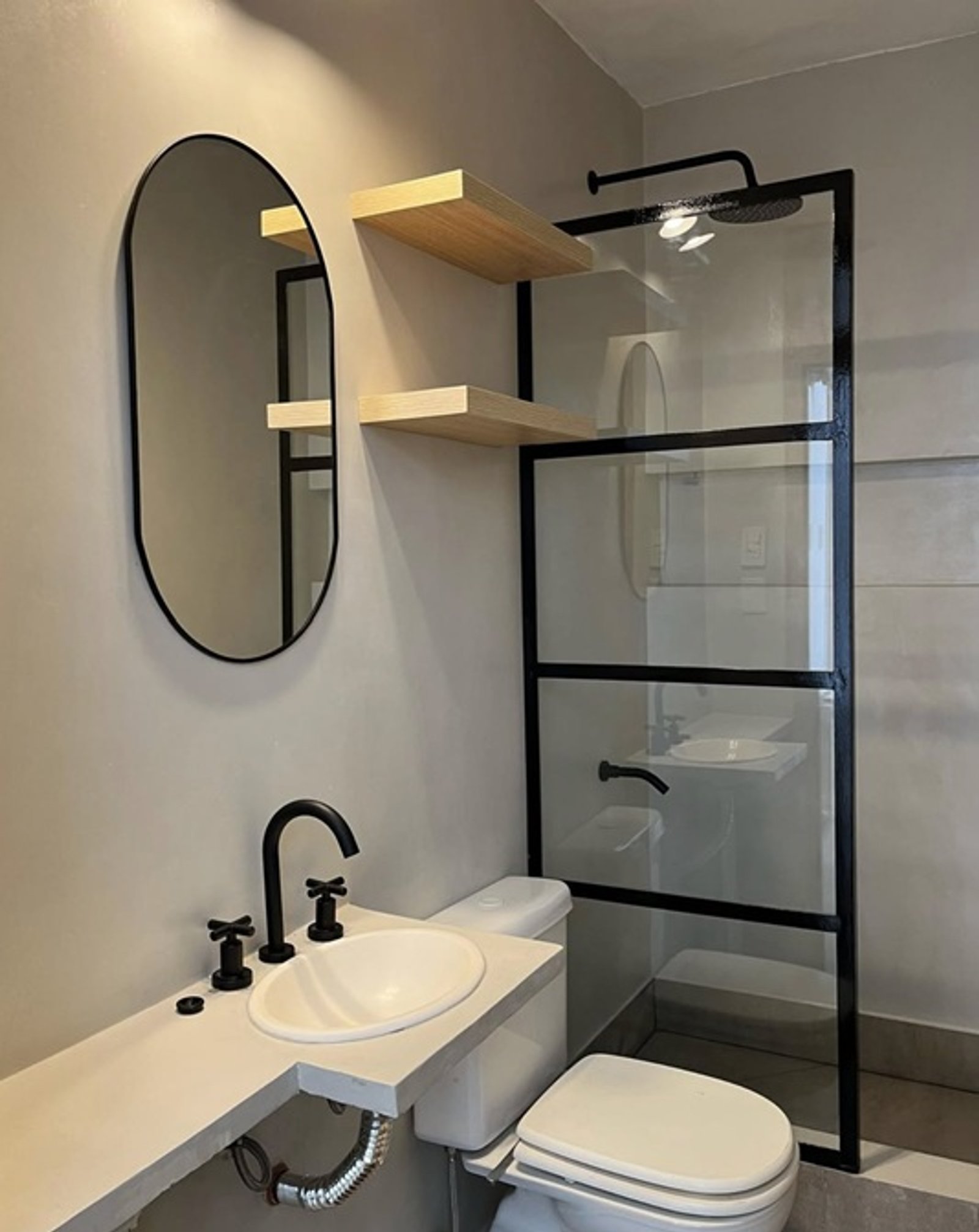 Baño moderno minimalista con espejo ovalado, estantes de madera y grifería negra — proyecto Carranza 2, por Estudio NET Arquitectura , en Adolfo P. Carranza 1931