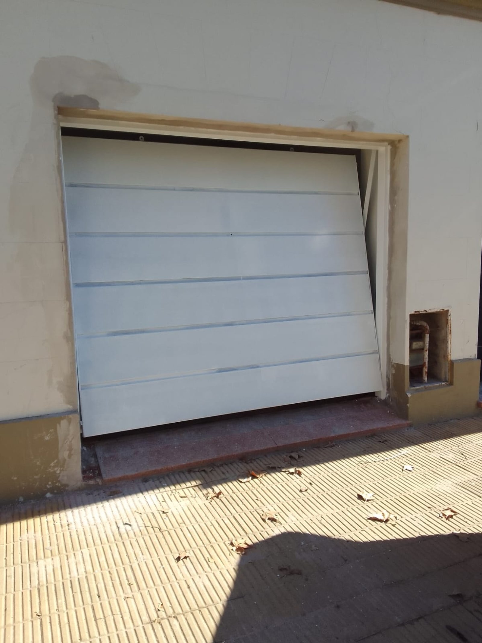 Portão de garagem branco semiaberto em fachada de concreto — projeto Casa en Banfield, por Arquitecto Guido Niccoli, em B1828 Banfield
