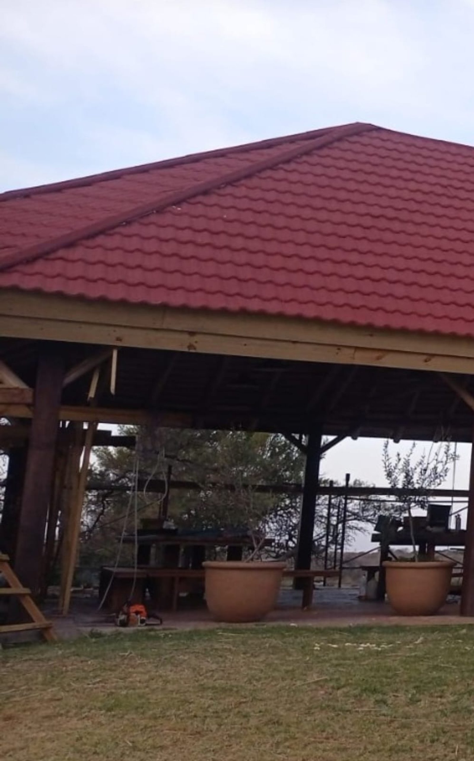 Pérgola rústica com telhado de telha metálica vermelha e vasos de terracota — projeto Teja Gravillada., por Yrigoyen Construcciones, em Córdoba
