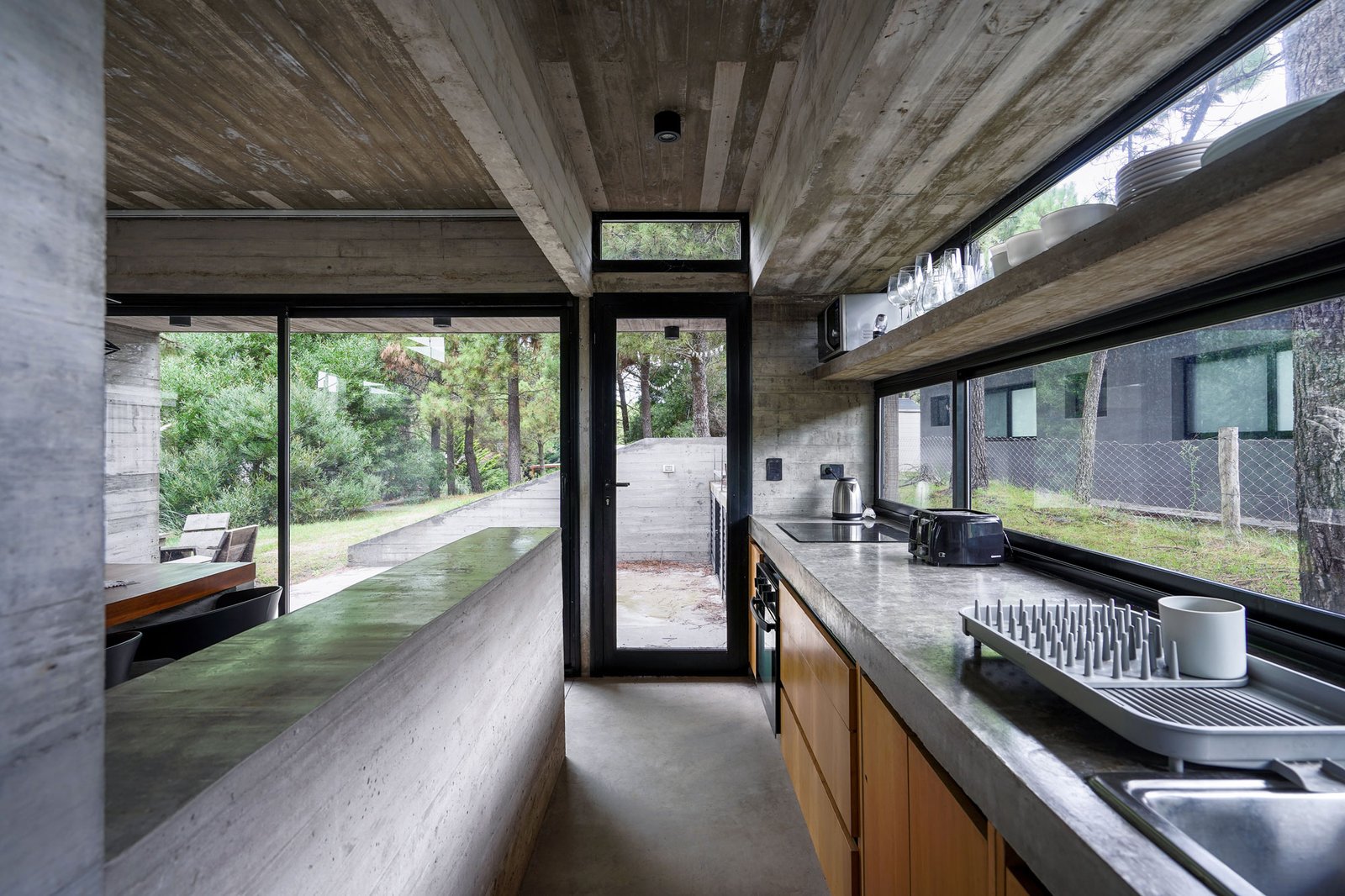 Cocina brutalista con isla de hormigón y vistas al bosque — proyecto Casa Loma, por Besonías Almeida arquitectos, en X6VF+67