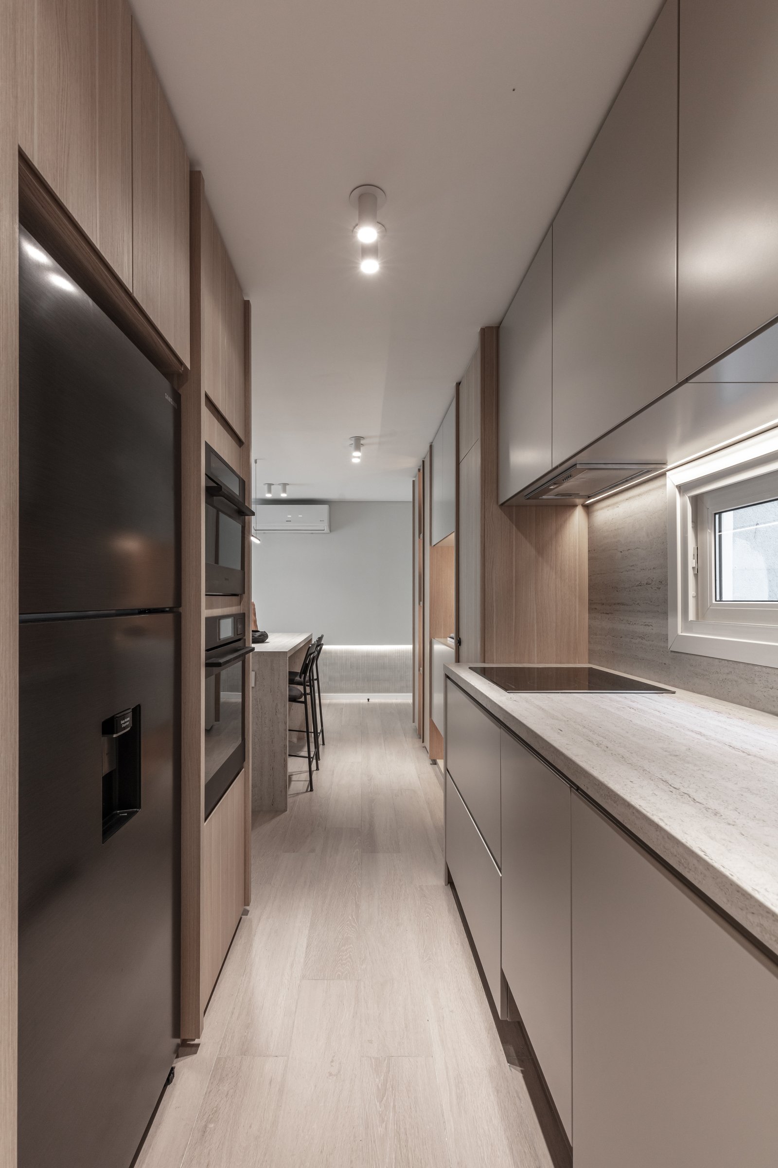 Cocina moderna y estrecha con gabinetes de madera y luz indirecta — proyecto Eslovenia | Pied-à-terre | Lucia Quinteros, por Ren Studio, en Cdad. Autónoma de Buenos Aires