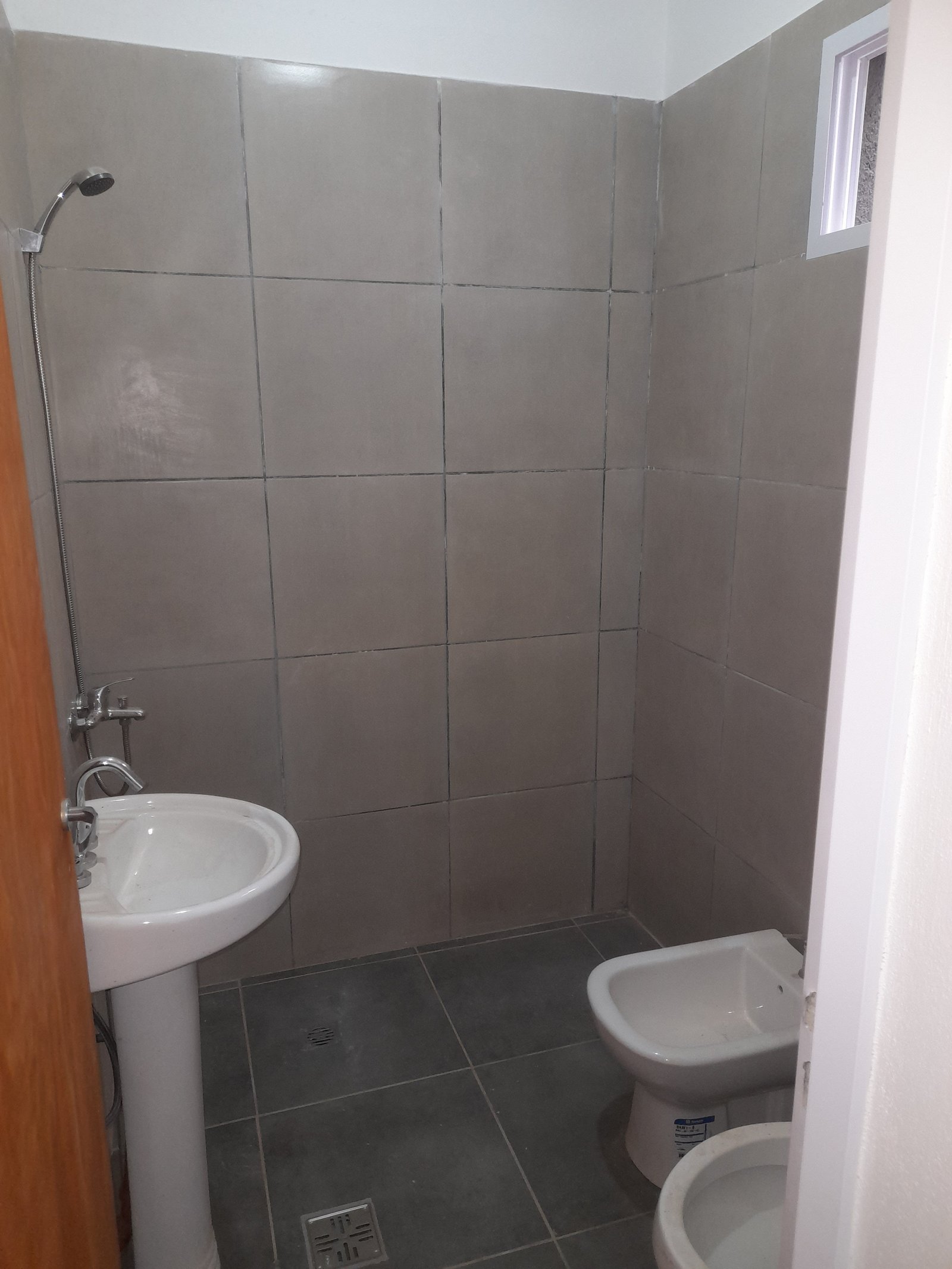 Banheiro moderno com azulejos cinzas, pia, vaso sanitário e bidê — projeto Departamentos, por CN Construcciones, em Alta Gracia