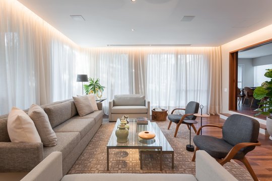 Living luminoso con ventanales, sofá gris y sillones de madera — proyecto Projeto MT Ipês, por Marta Calasans