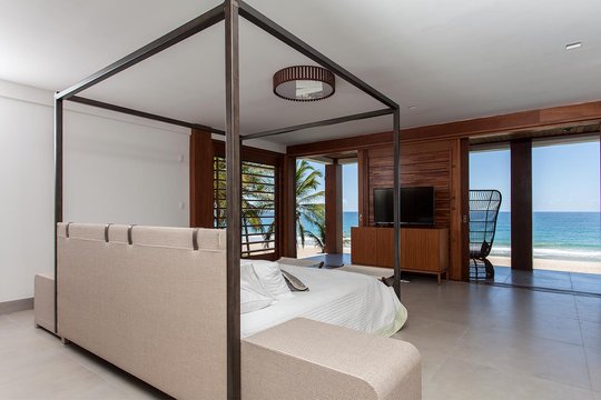 Dormitorio con cama dosel frente al mar y acabados de madera — proyecto Residência CM, por Milcent Arquitetura