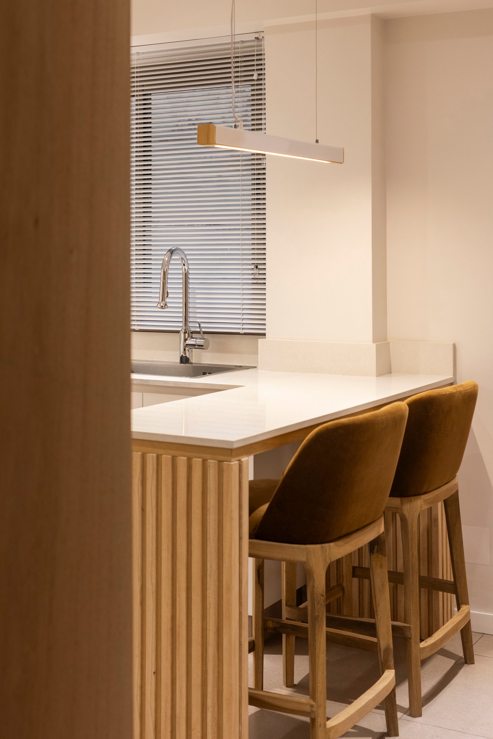Cocina moderna con isla de madera, barras de terciopelo y luz colgante lineal — proyecto BARRACAS, por La Nave Arq., en Barracas