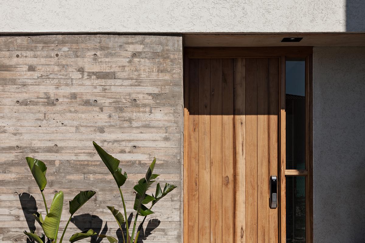 fachada moderna com concreto texturizado e porta de madeira — projeto CASA RDV, por Rastro Estudio, em San Isidro