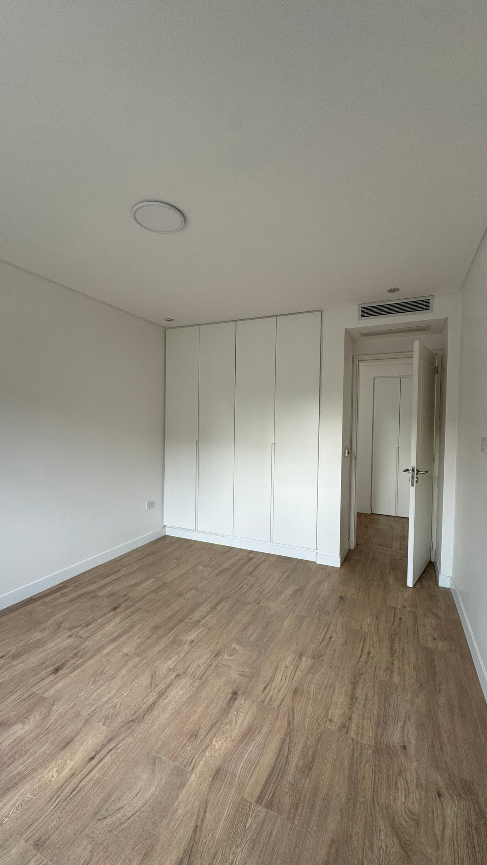 dormitorio minimalista con amplios placares blancos integrados y piso de madera — proyecto Casa MC, por Hermann Arquitectos, en Bv. Central