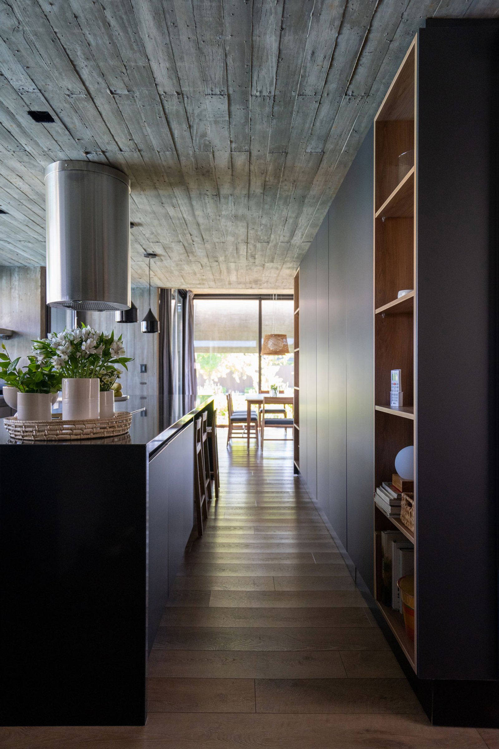 Corredor moderno com teto de concreto aparente e prateleiras de madeira escura — projeto Casa Tres Patios, por Besonías Almeida arquitectos, em Pilar