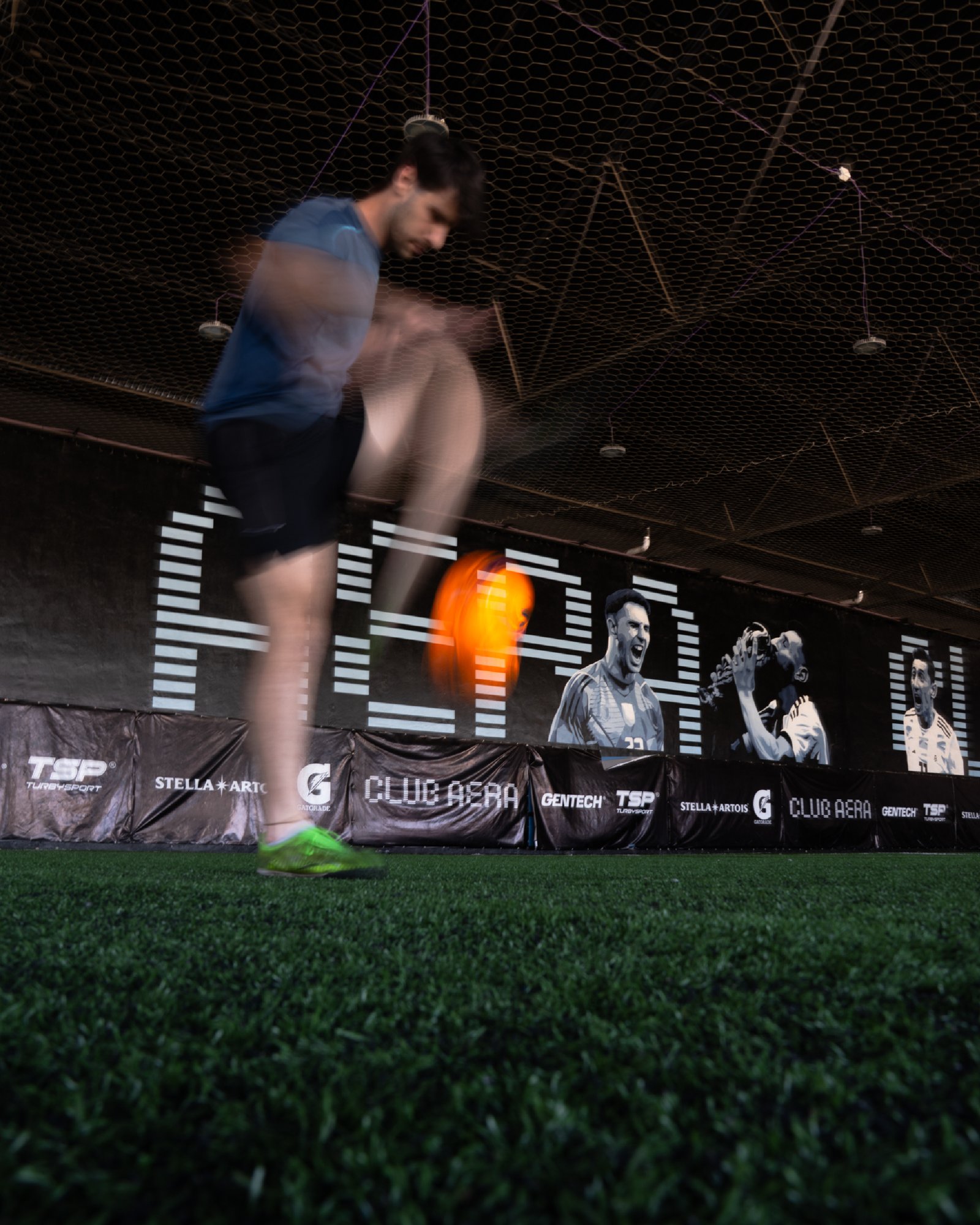 Jogador de futebol em movimento em quadra coberta com painéis de retratos — projeto CLUB AERA, por UN.MURAL, em Villa Lynch