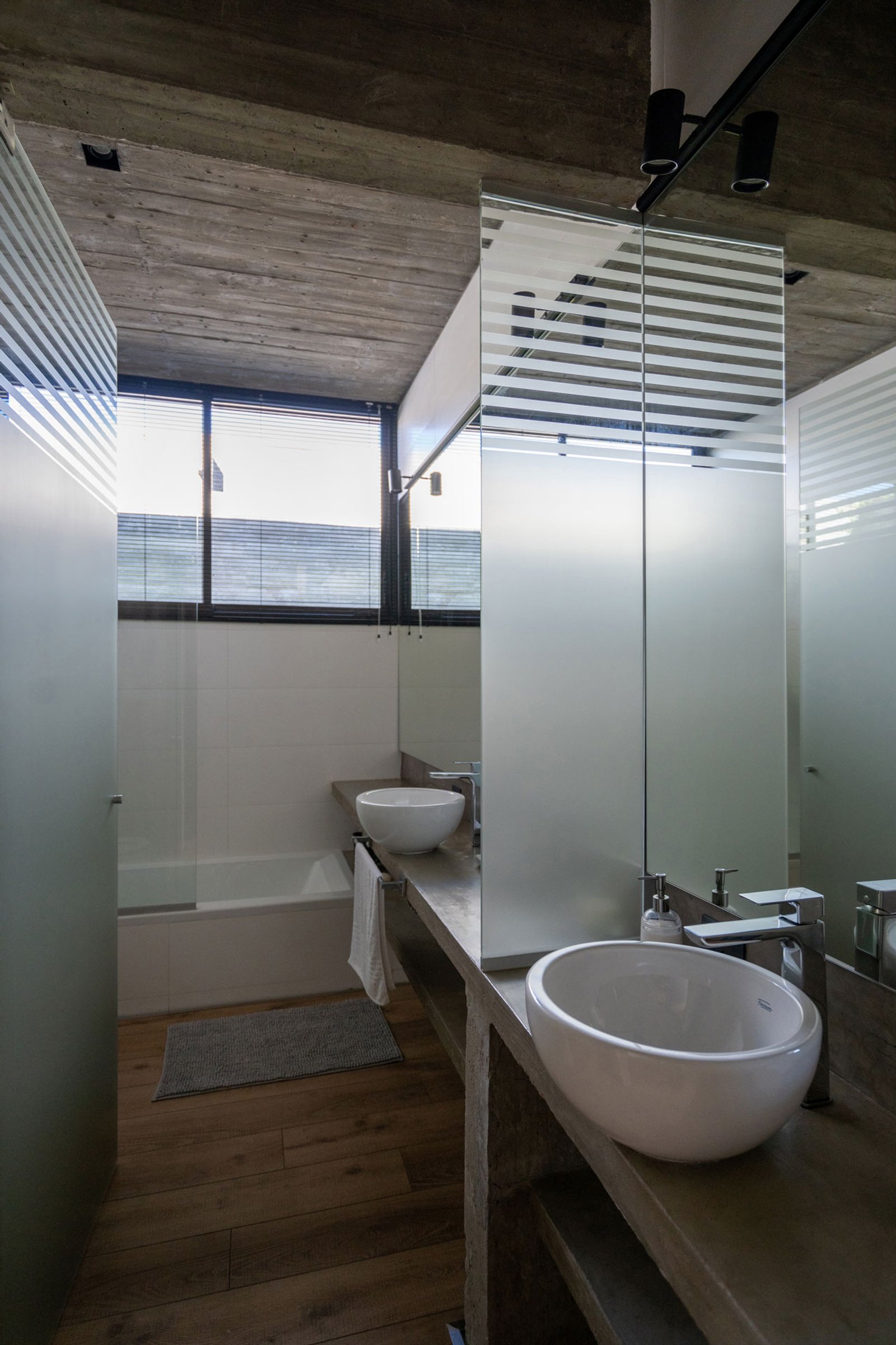Banheiro moderno com teto de concreto, divisórias de vidro fosco e cuba sobre bancada — projeto Casa Tres Patios, por Besonías Almeida arquitectos, em Pilar