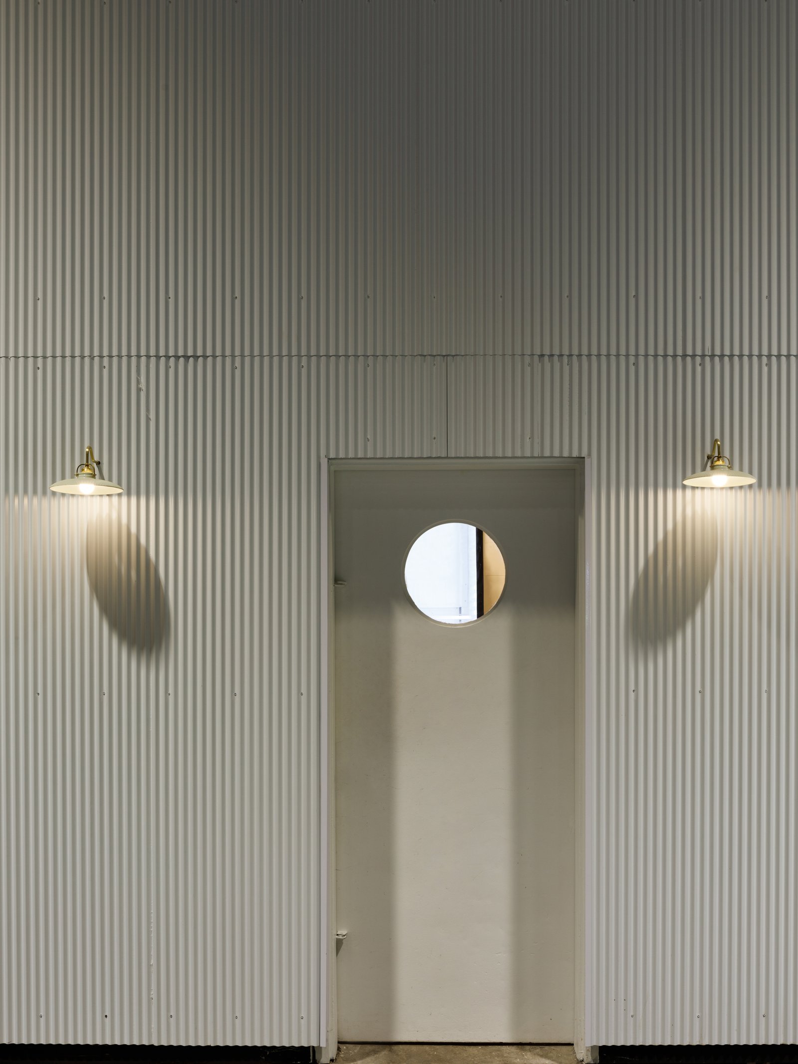 Paredes de metal corrugado con luces industriales y espejo redondo — proyecto RUTH La Rural, por Estudio Losa, en Juncal 4431