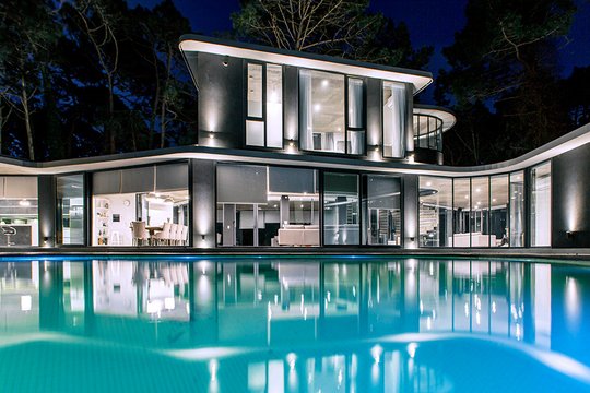 Moderna casa con piscina infinita de noche en un bosque — proyecto Casa Ameba, por MUCHTEK, en B7167 Cariló
