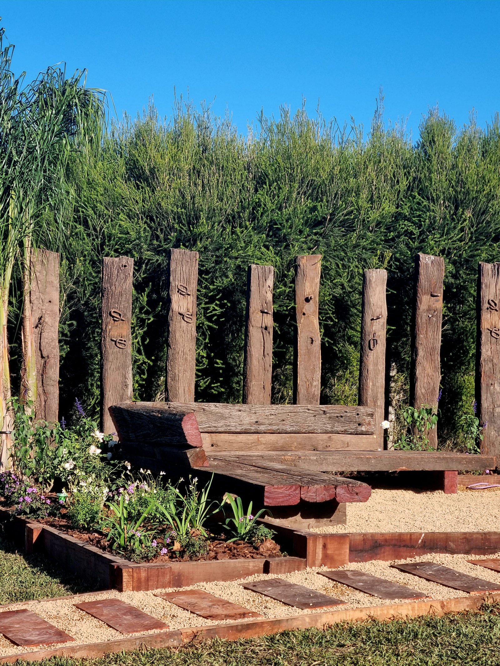 Banco rústico de madeira de demolição em pátio com jardim e plantas — projeto Barrio El Cantón Islas, por Marcela García Brünner Paisajista, em Calle Libertad 310 and Av. San Marti