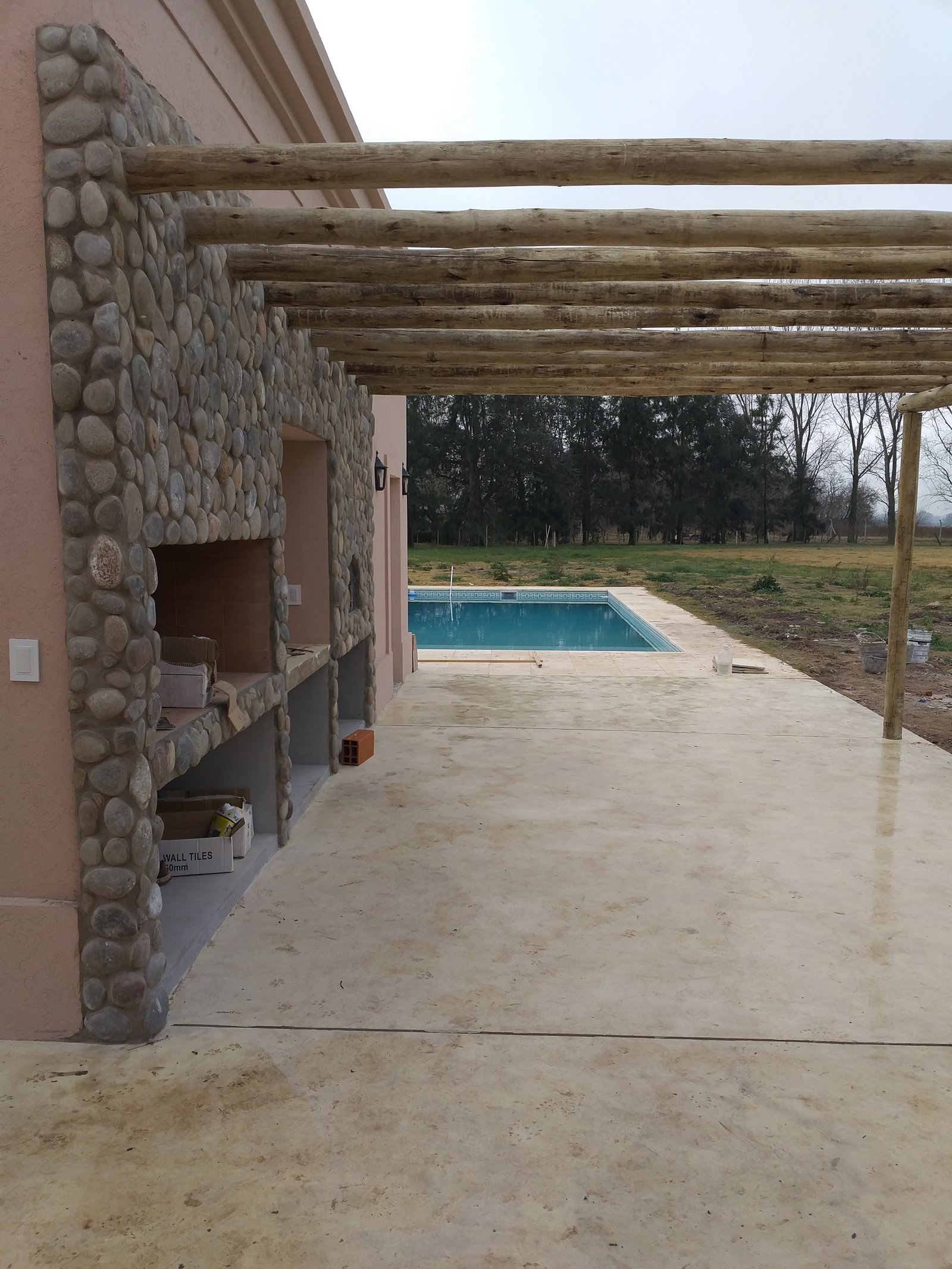 Quincho rústico con parrilla de piedra y pérgola de troncos — proyecto Casa de Campo, por Estudio Fernandez Long & asoc., en San Andres de Giles