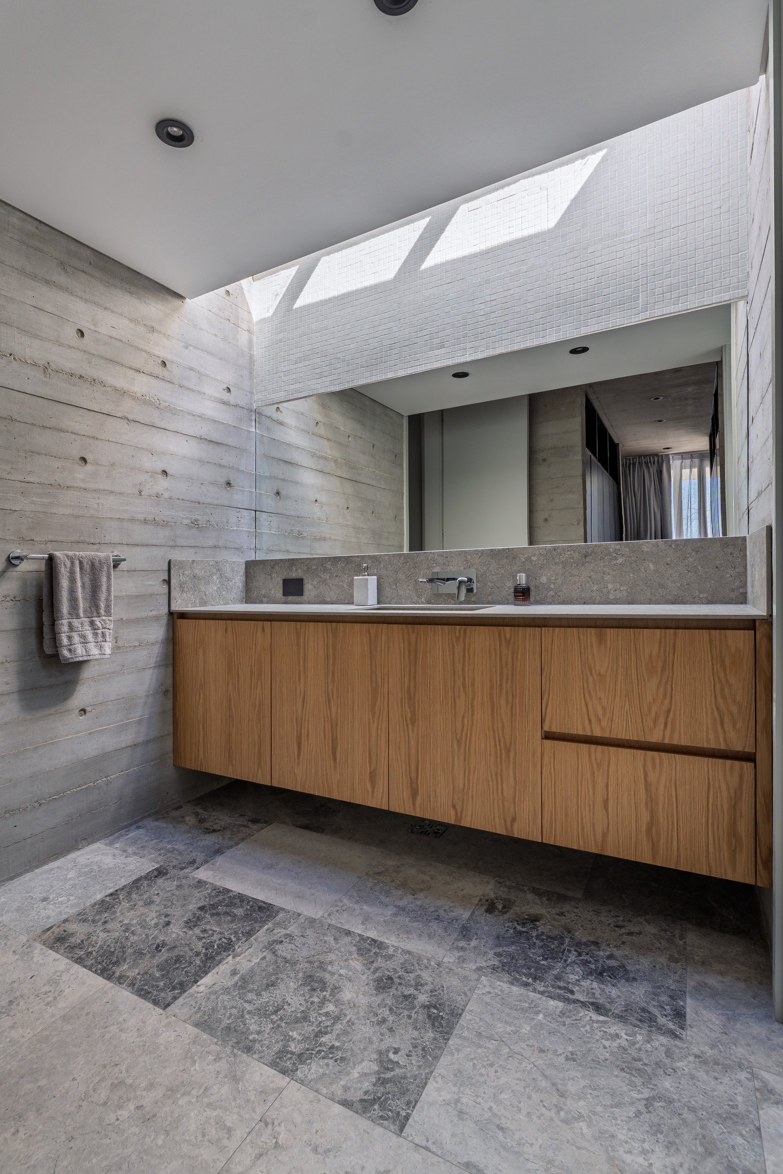 Banheiro moderno com paredes de concreto, claraboia e gabinete de madeira flutuante — projeto La Martona - Estudio Barcelona, por ABEJA CONCEPT, em Cañuelas