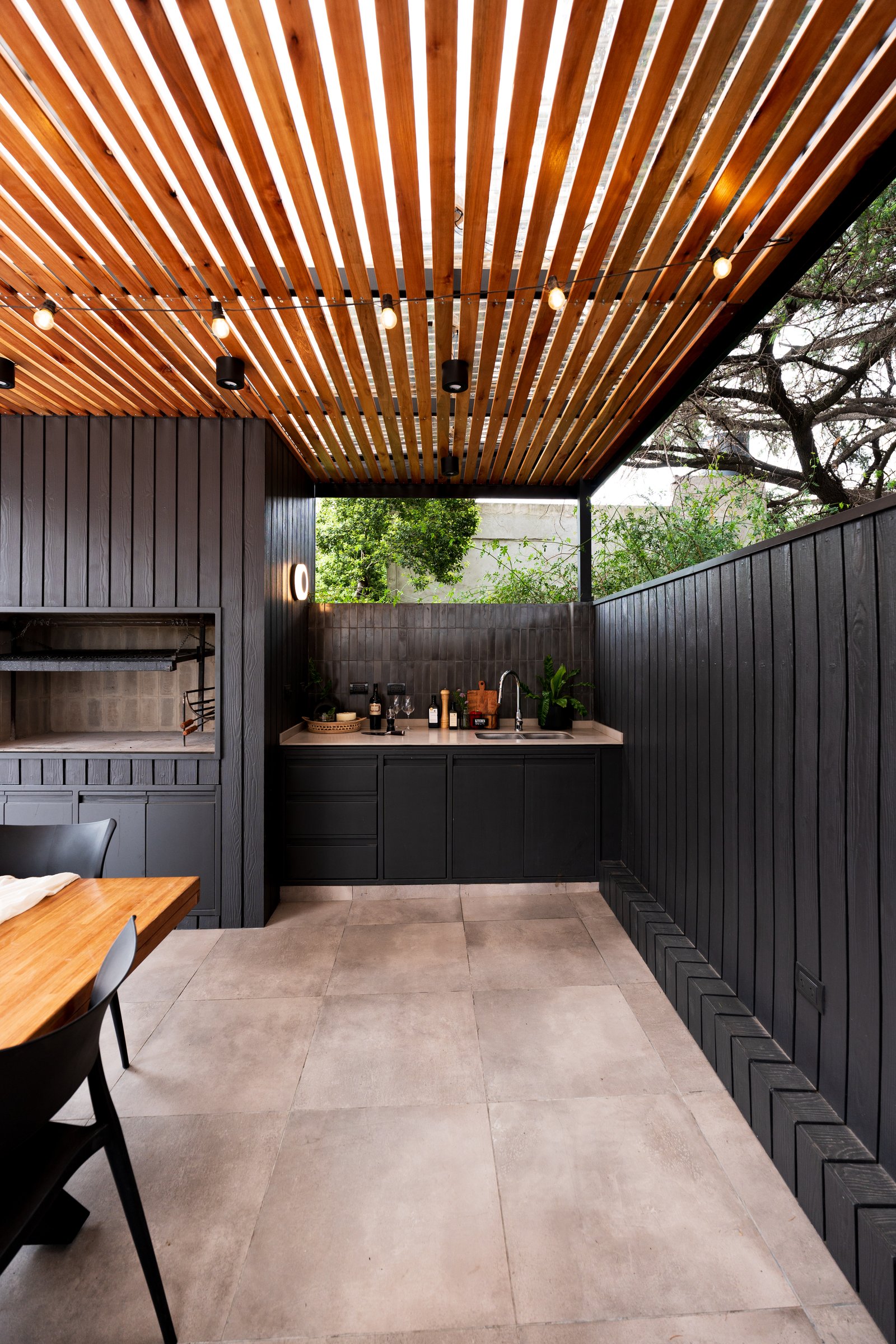 quincho moderno con pérgola de madera y cocina negra — proyecto TERRAZA MARCOS SASTRE, por FARQ ESTUDIO, en Villa del Parque