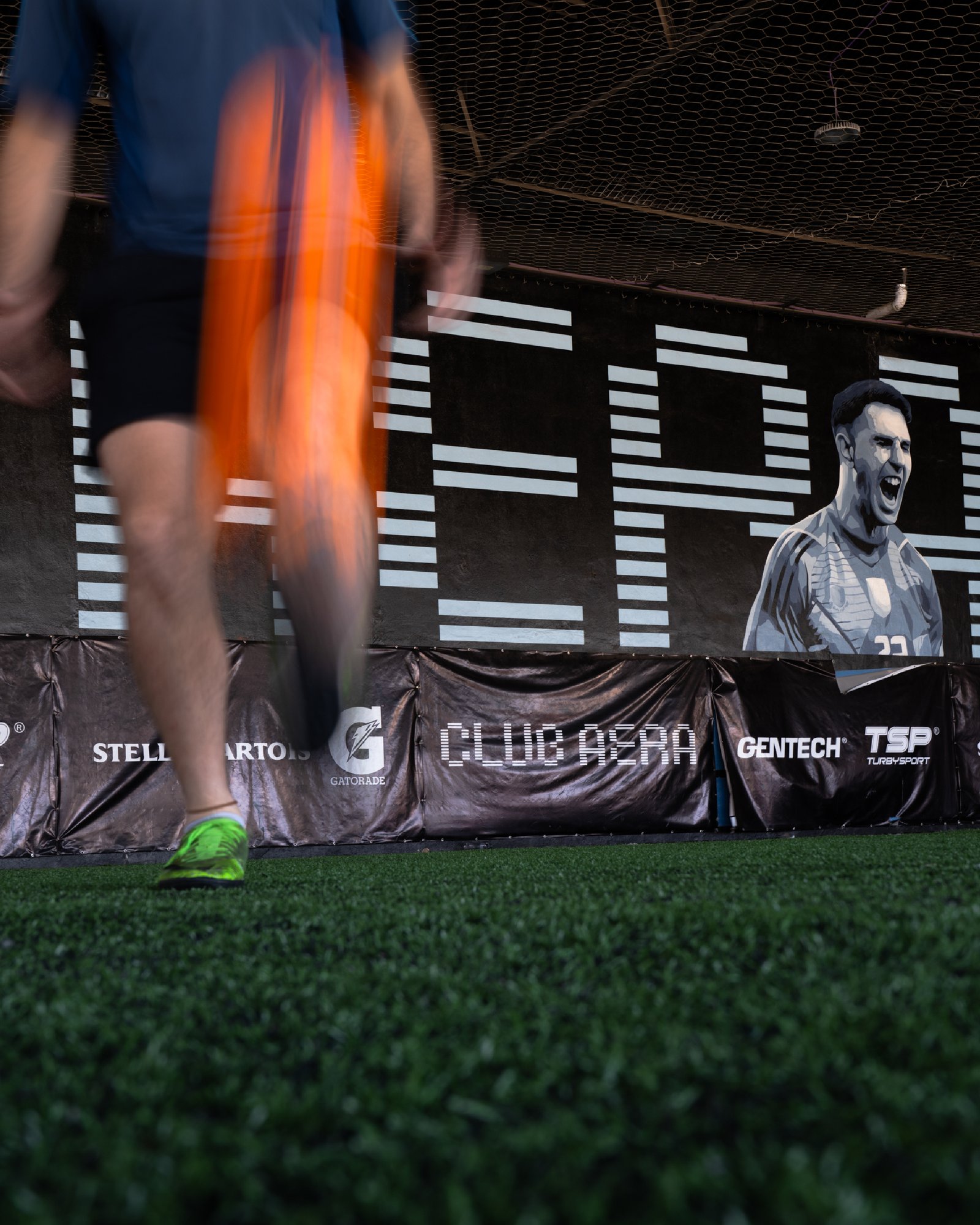 campo de futbol artificial con mural de futbolista — proyecto CLUB AERA, por UN.MURAL, en Villa Lynch