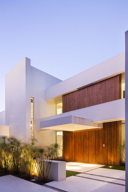 Fachada moderna minimalista con madera y iluminación cálida — proyecto Modernismo Náutico, por Apaarquitectura, en Tigre