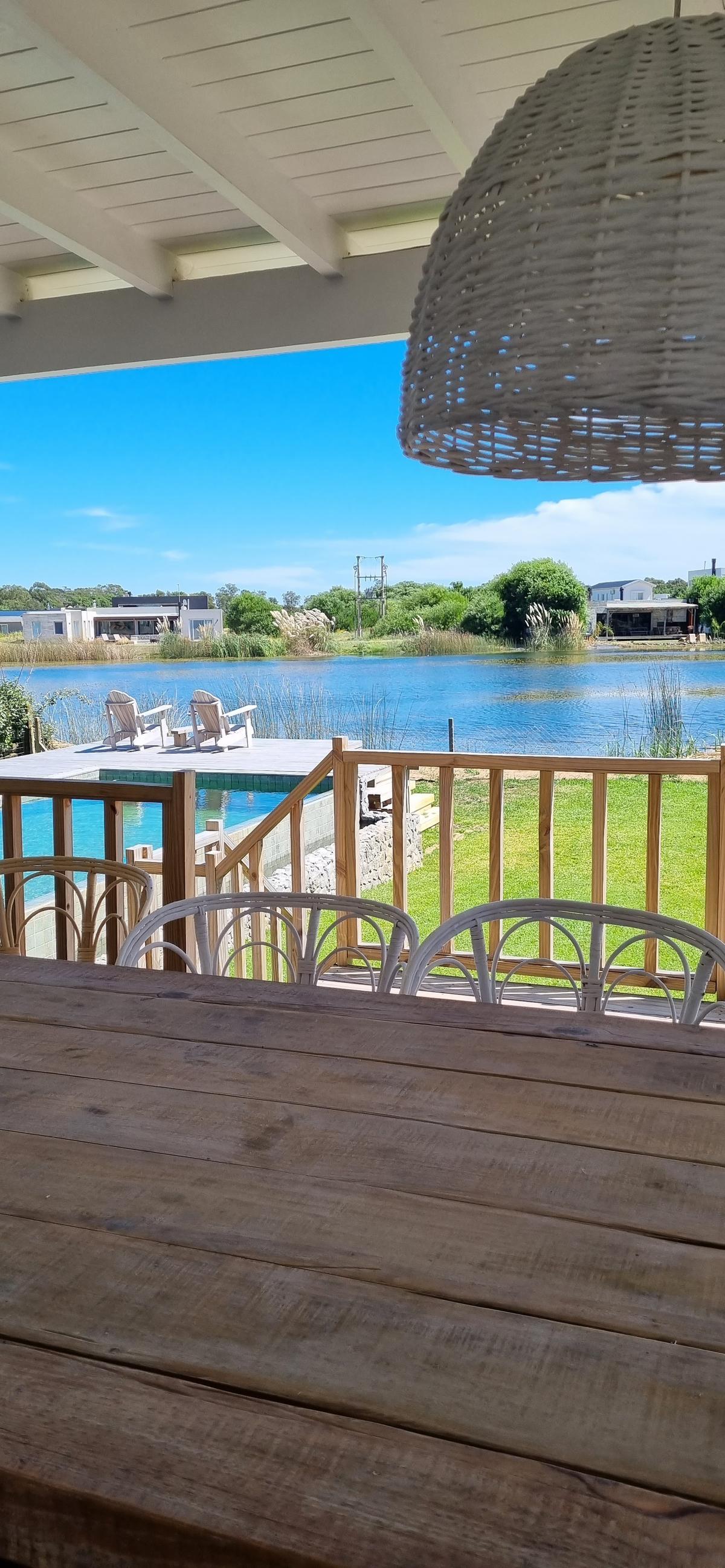 Sala de jantar externa com vista para lago e piscina — projeto Casa costa, por Trazarq, em Pinamar