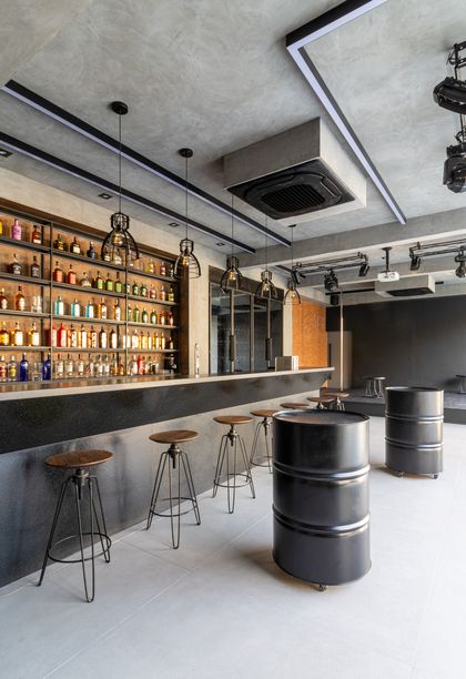 Bar industrial con barriles y estantes de licores, techo de hormigón — proyecto Mansão de Gabigol, por Carlos Pardal, en Guarujá