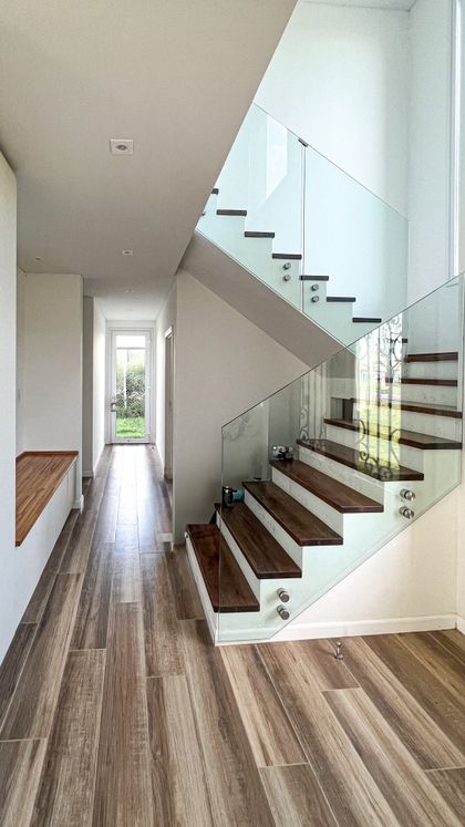 Escalera moderna con pasamanos de vidrio, piso de madera oscura y luz natural — proyecto Casa Hipico, por RY Construir Estudio, en Pilar
