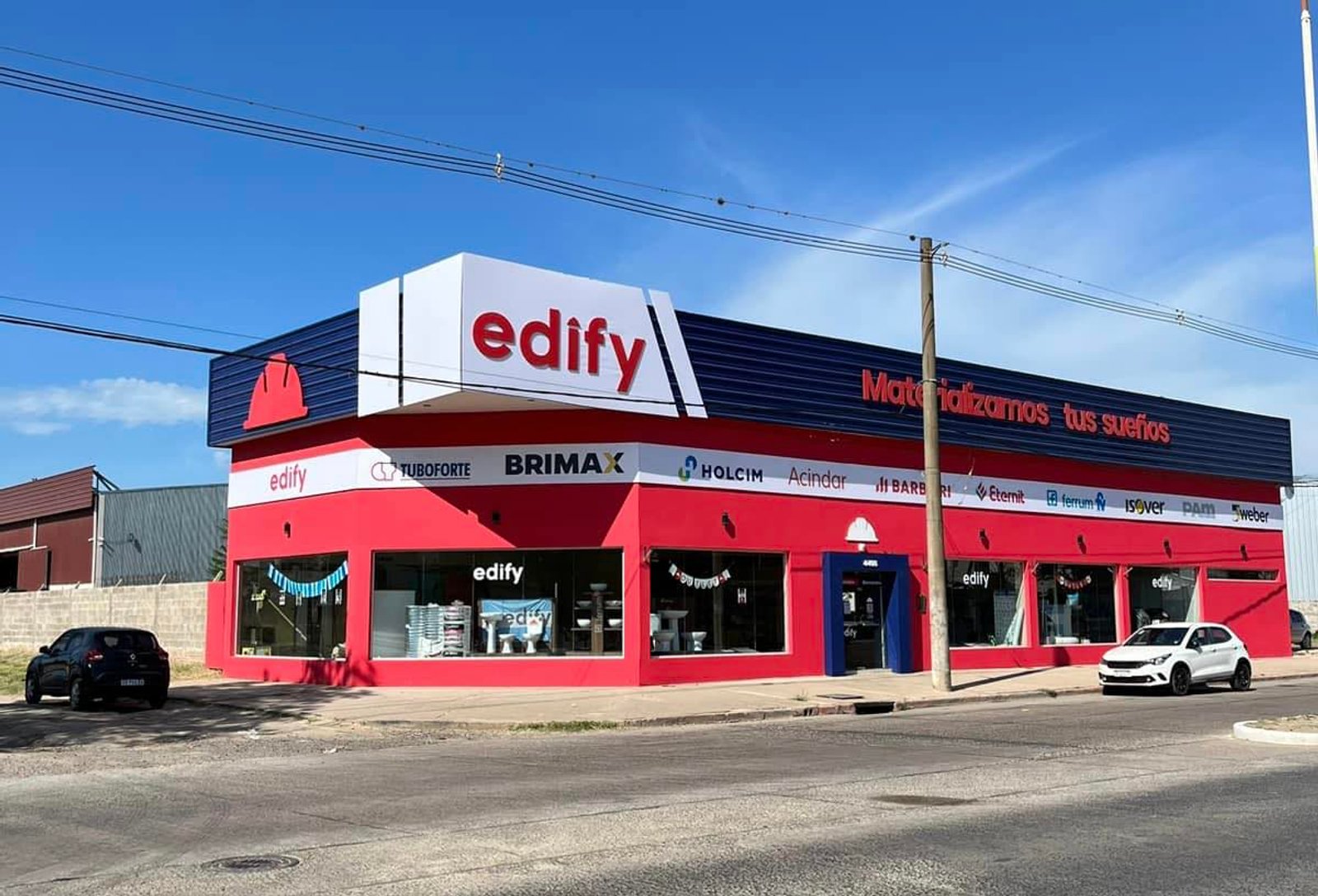 Fachada de edifício comercial moderno, vermelho e azul, com carros na frente — projeto Edify Corrientes, Casa de Materiales de Construccion., por Arquitecto Gustavo Maidana, em Cor