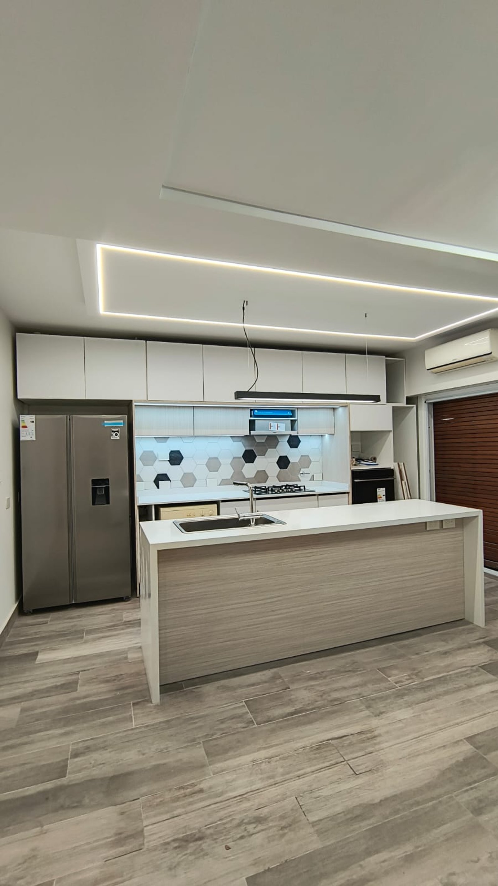 Cocina moderna con isla grande, gabinetes blancos y piso de madera gris — proyecto Emmet Brown, por Plasma co, en Buenos Aires