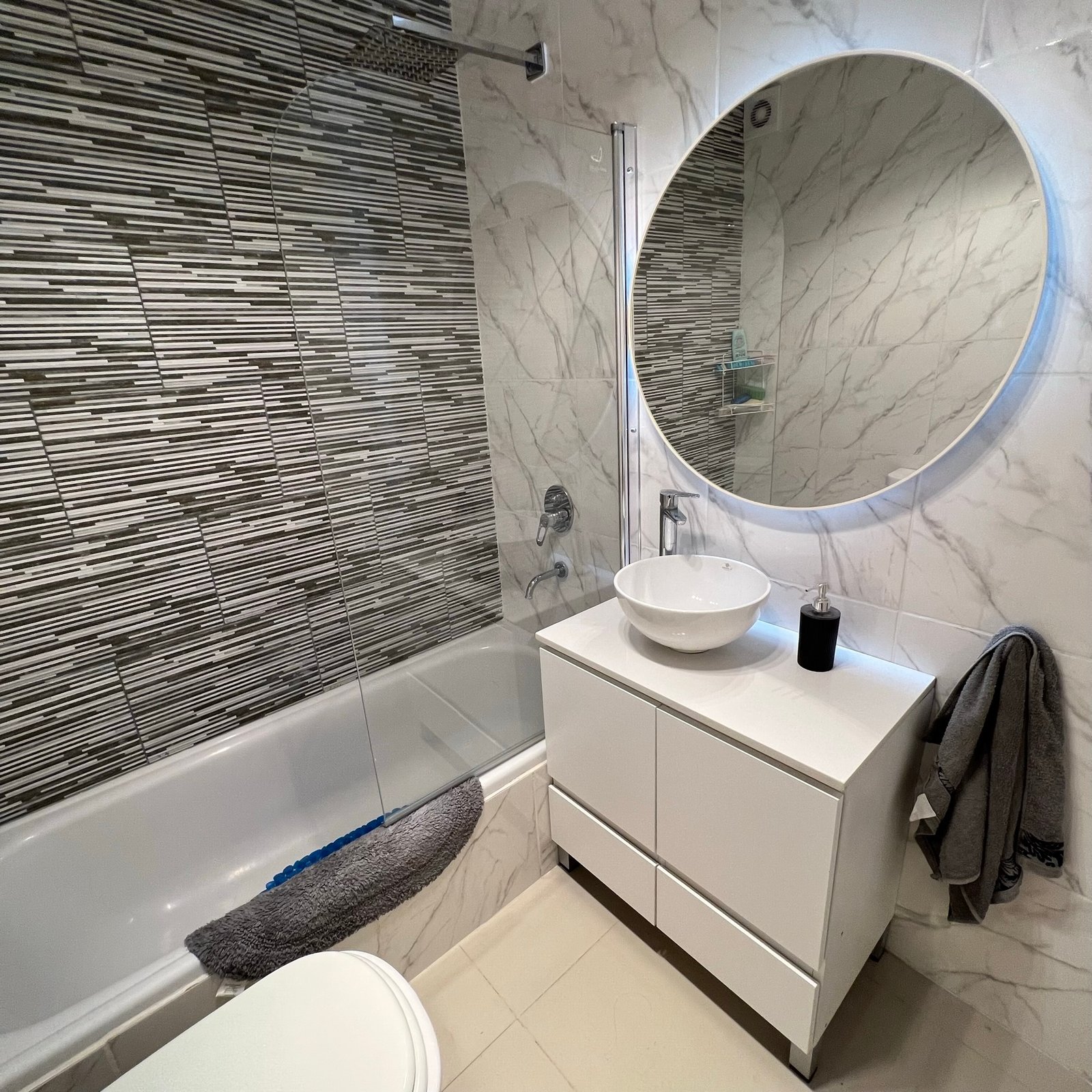 Baño moderno con espejo redondo retroiluminado y vanitory blanco — proyecto Epuyen II, por MDBK Arquitectura, en Caballito